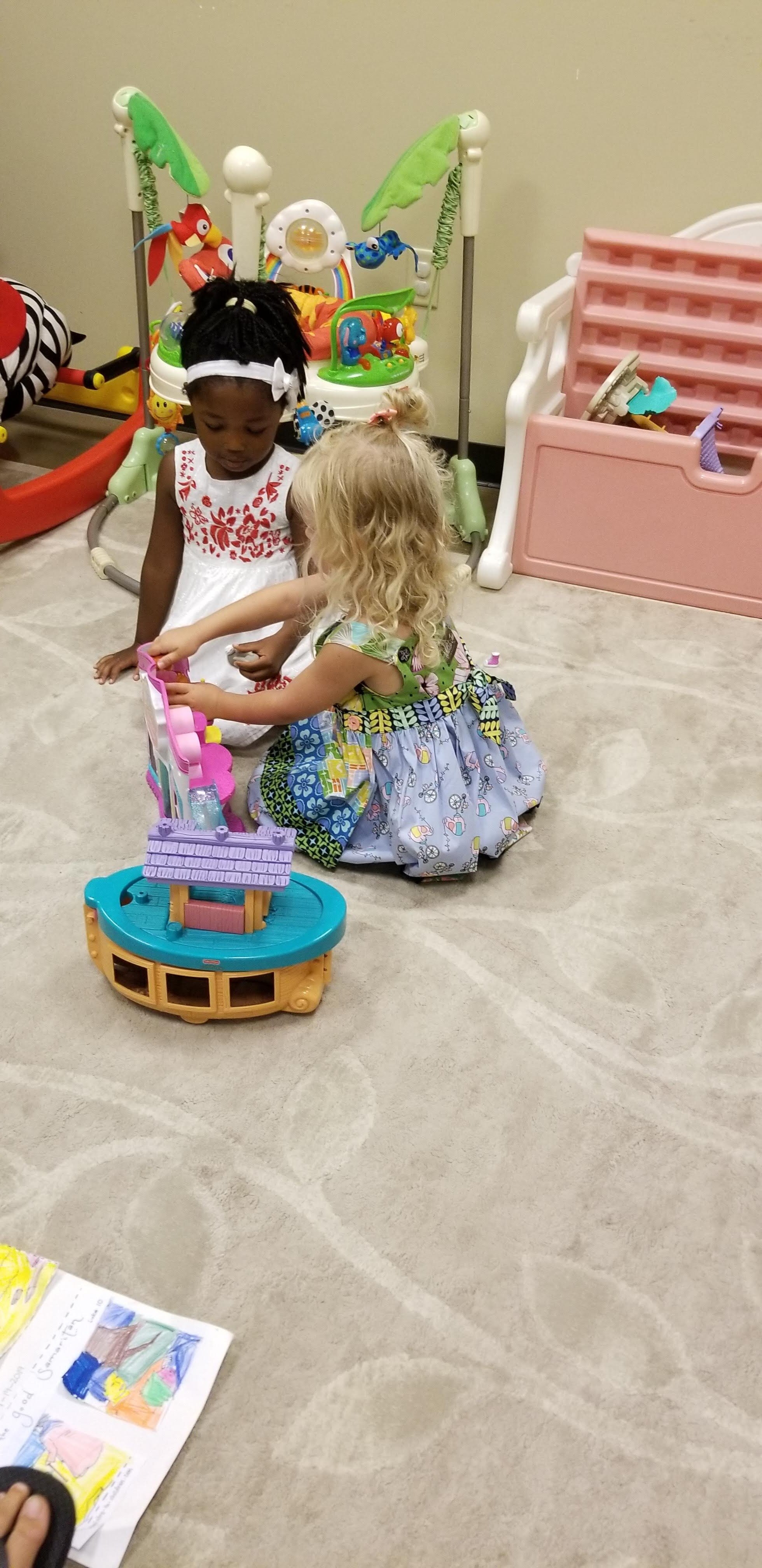 Two children playing with a toy boat on a carpet in a play area, surrounded by colorful toys and equipment.