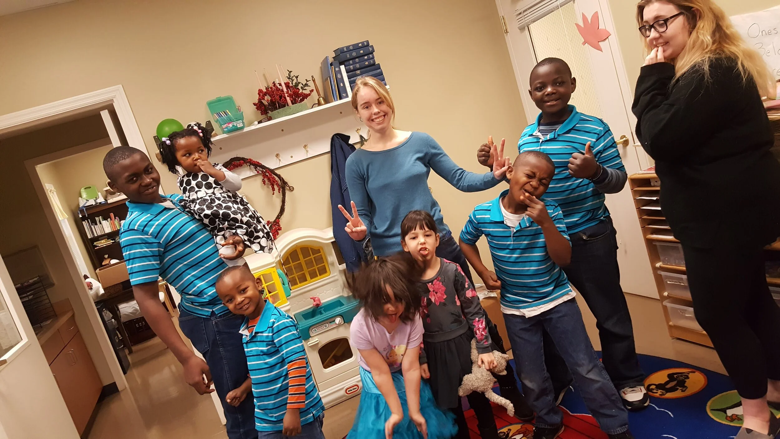 Group of adults and children posing in a classroom with colorful decor and toys.