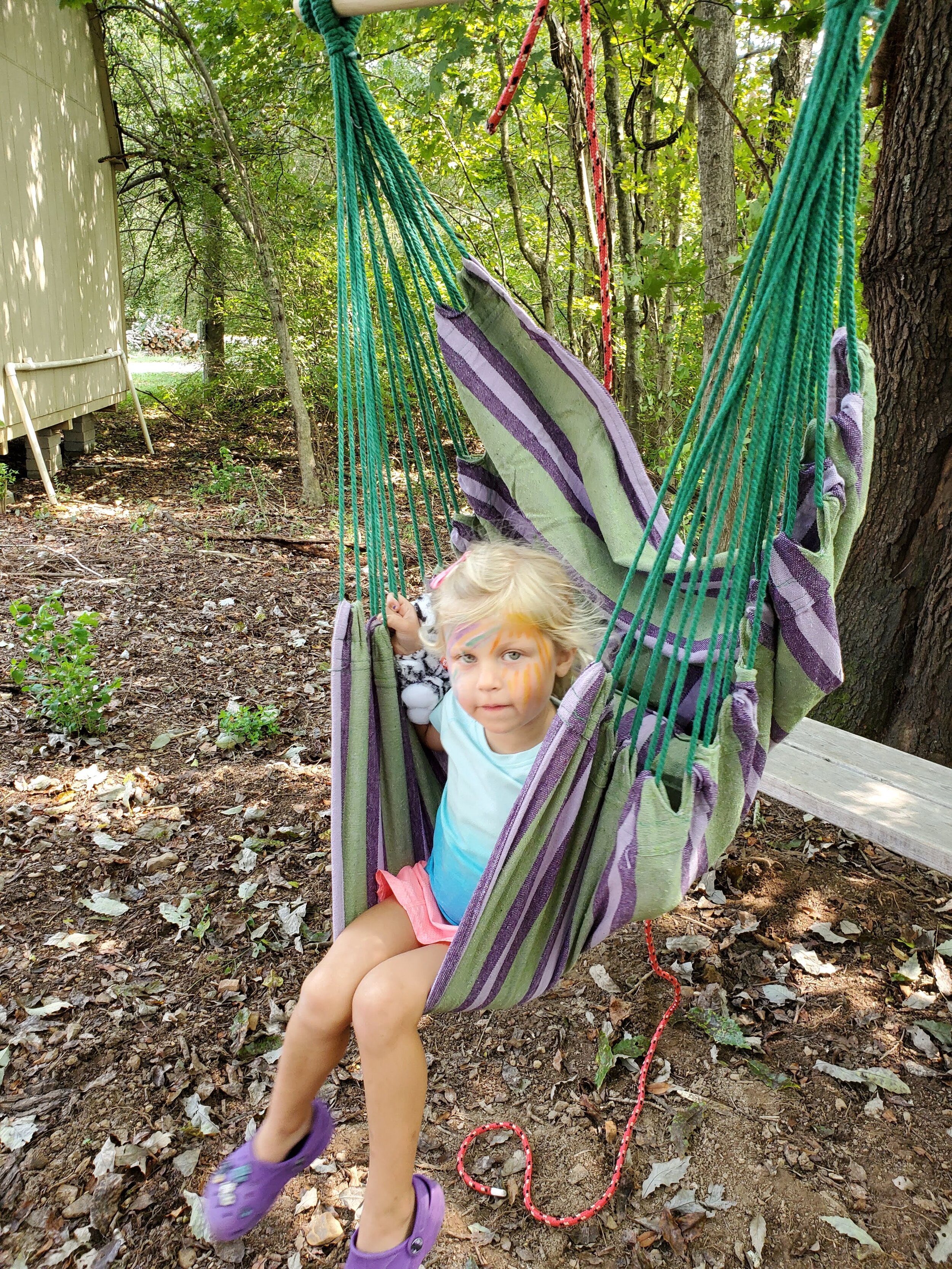 Child sitting in a striped hammock swing in a wooded area.