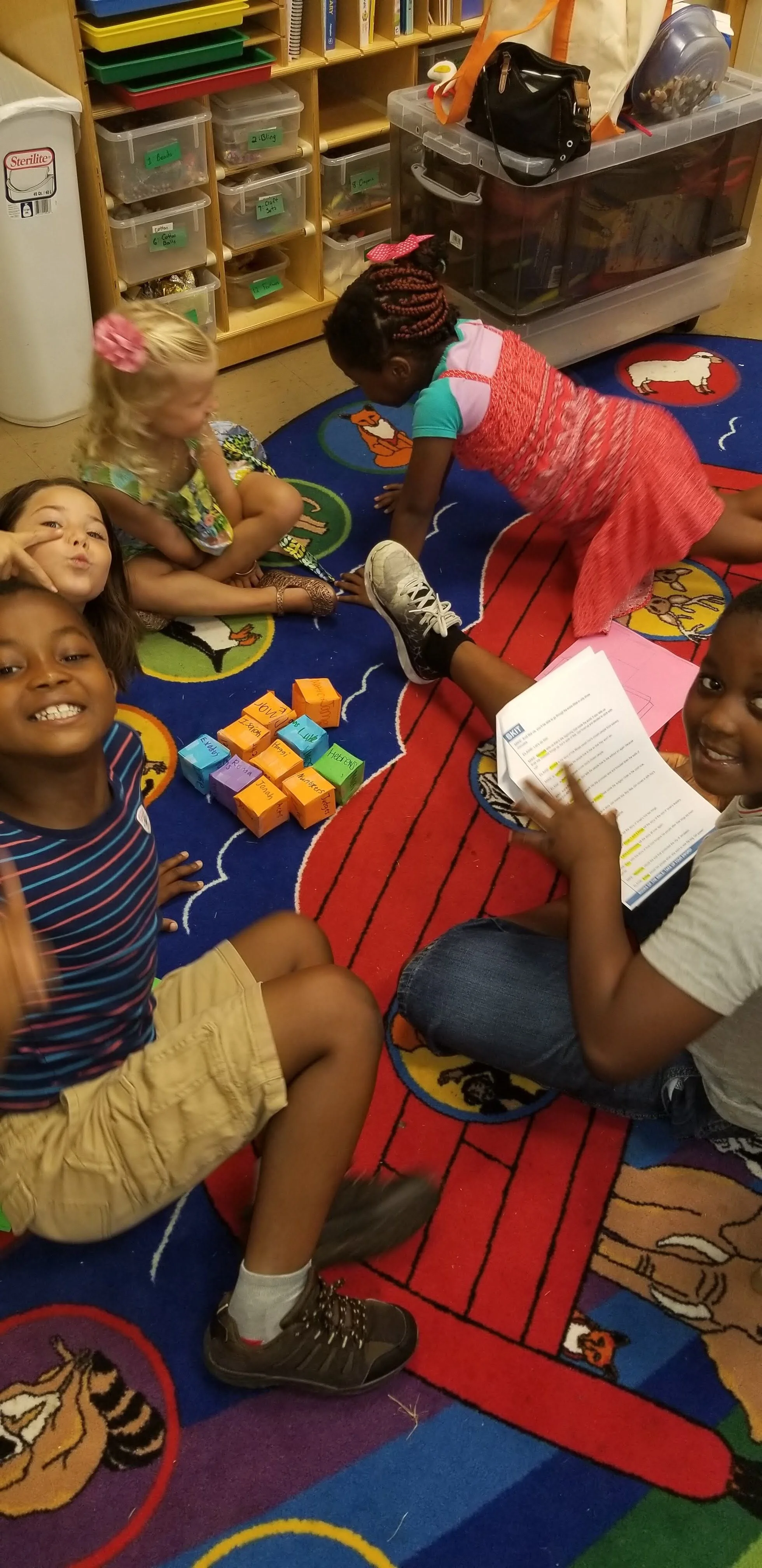 Children sitting on a colorful rug in a classroom, playing with paper blocks and reading papers.