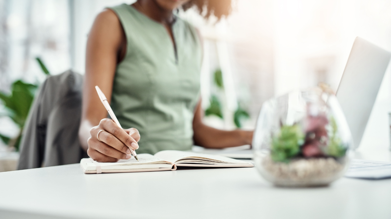 Woman writing in notebook while sat at desk
