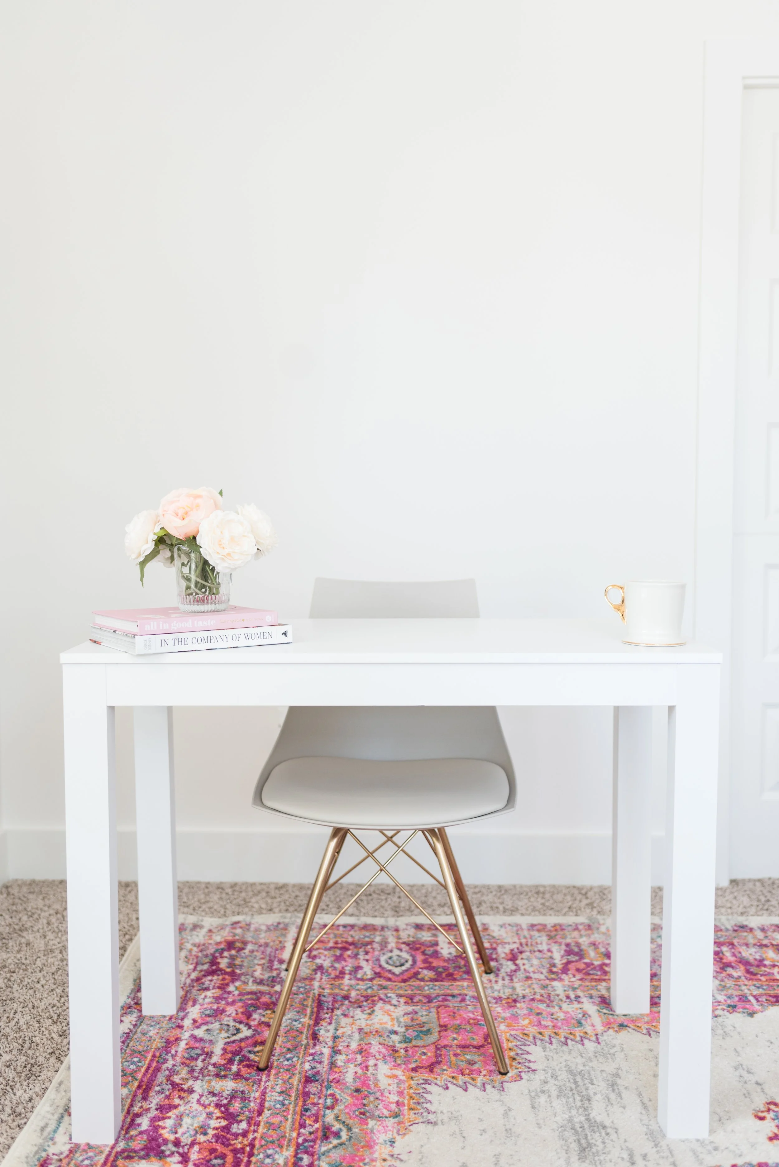 Southern California Brand Photographer Sharon Wallace Photography white desk pink rug brand desk with vase of flowers, white chair, and white walls. Portrait studio brand photography. female office desk.