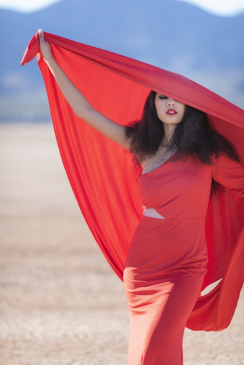 Editorial senior portrait with flowing red fabric against a blue desert sky in Southern California.