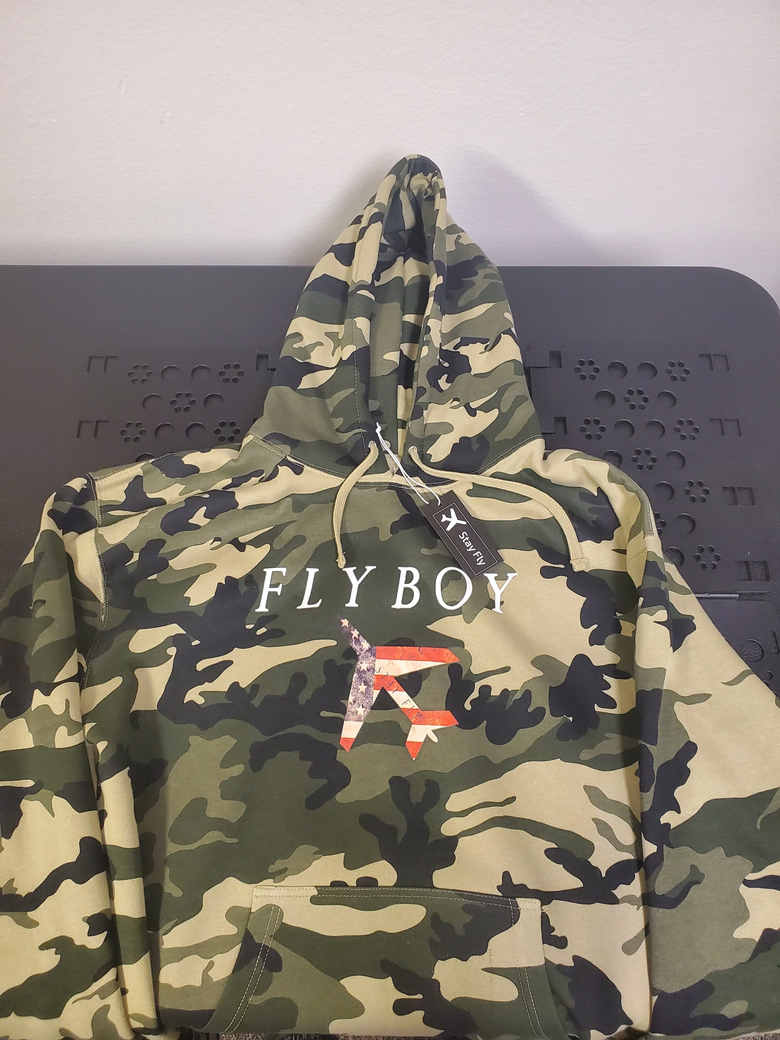 Camouflage hoodie with 'FLYBOY' and a stylized graphic of a flying horse, hanging on a black surface.