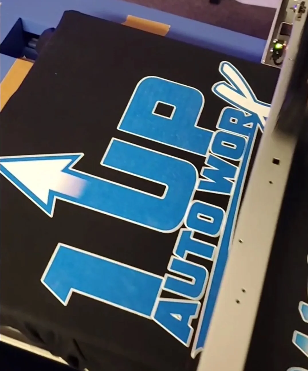 Close-up of a sign with blue and white text that reads "JDR AUCTION WORLD" on a black background, with a large blue arrow pointing left.