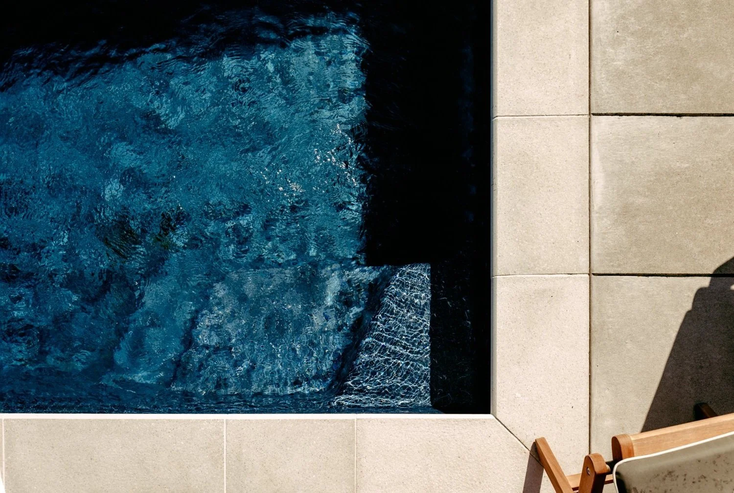 Close-up of a contemporary concrete pool surround with sleek tiling, showcasing clear blue water and modern outdoor furniture by Auckland Concrete Layers.