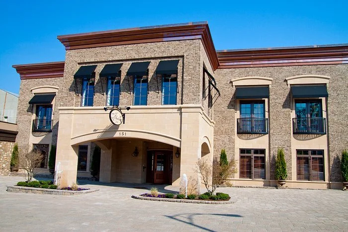 Exterior of a brick building with arched entryways, balconies, and a clock sign.