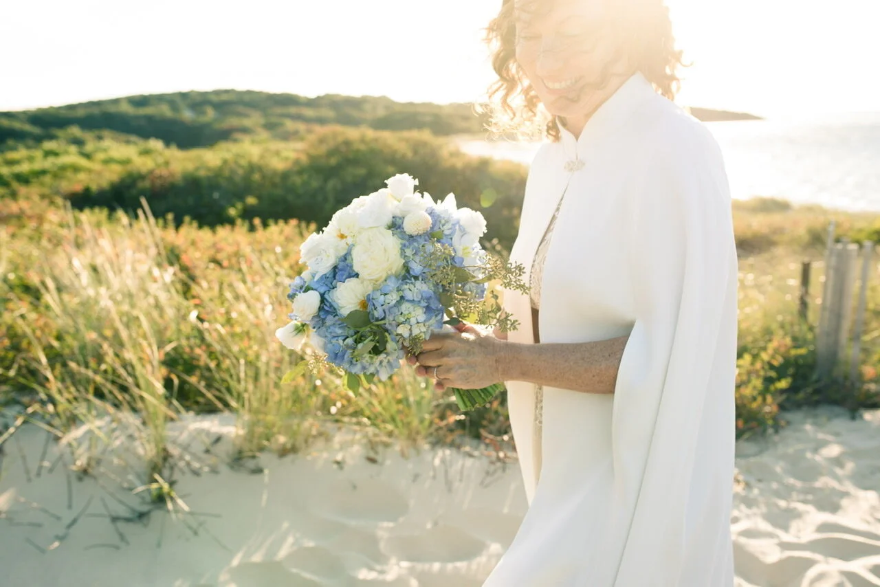 Bride wearing white with a blue and white bouquet on beach