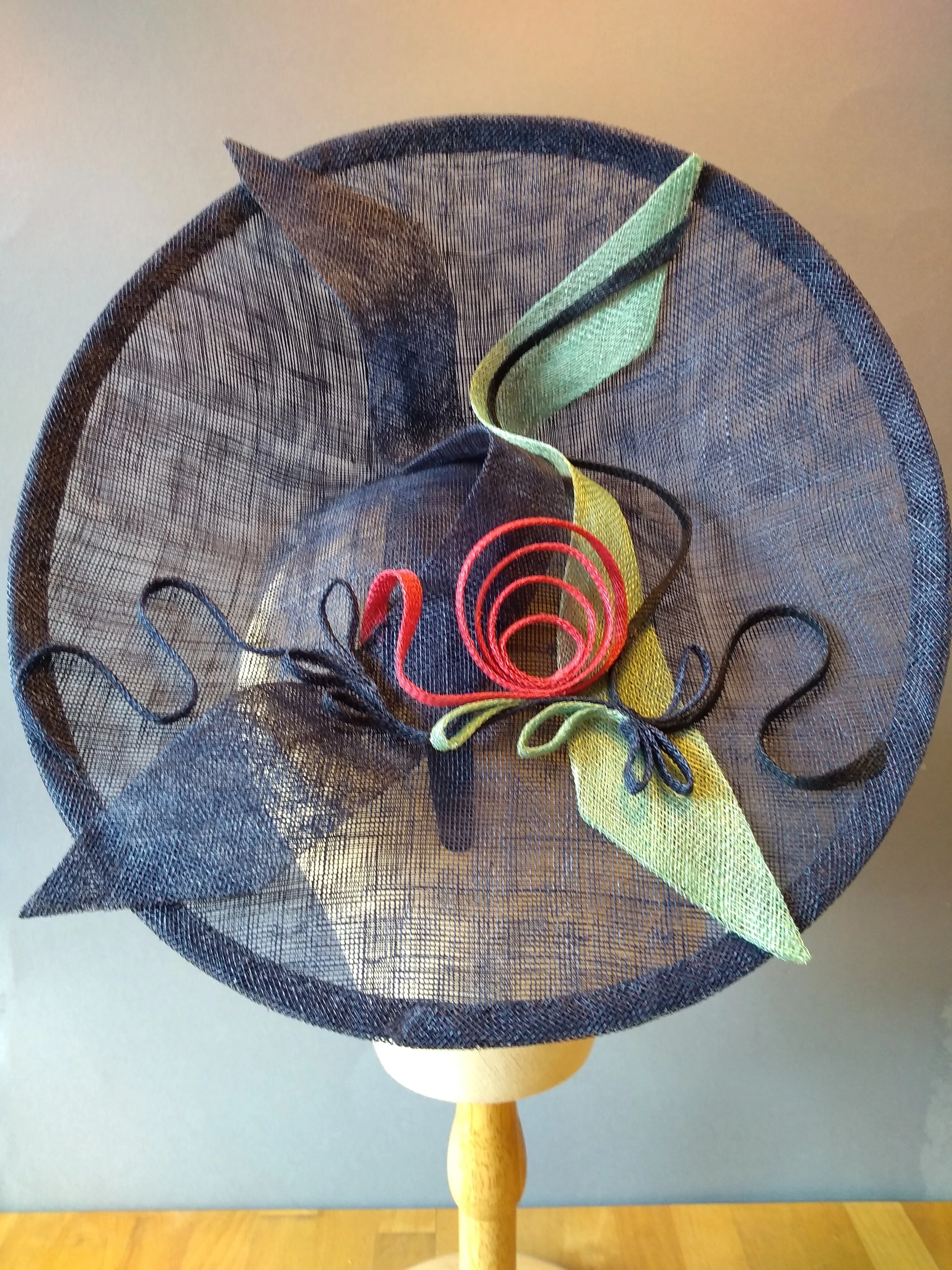 Dramatic saucer headpiece made from dark blue sinamay, with accents of pink and mint green.