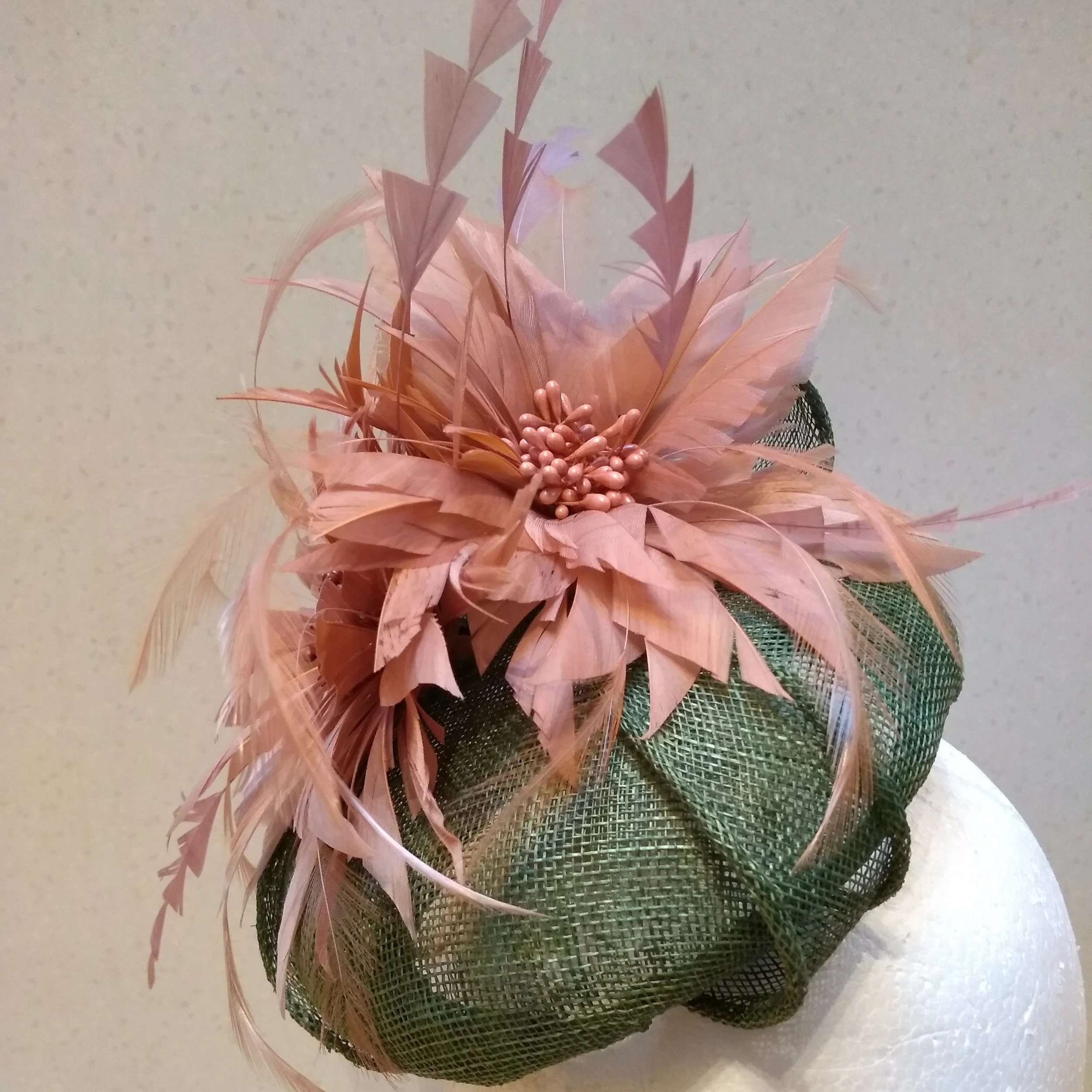 Green sinamay perching hat with dynamic feather flowers and trimmed feathers in dusky pink. 