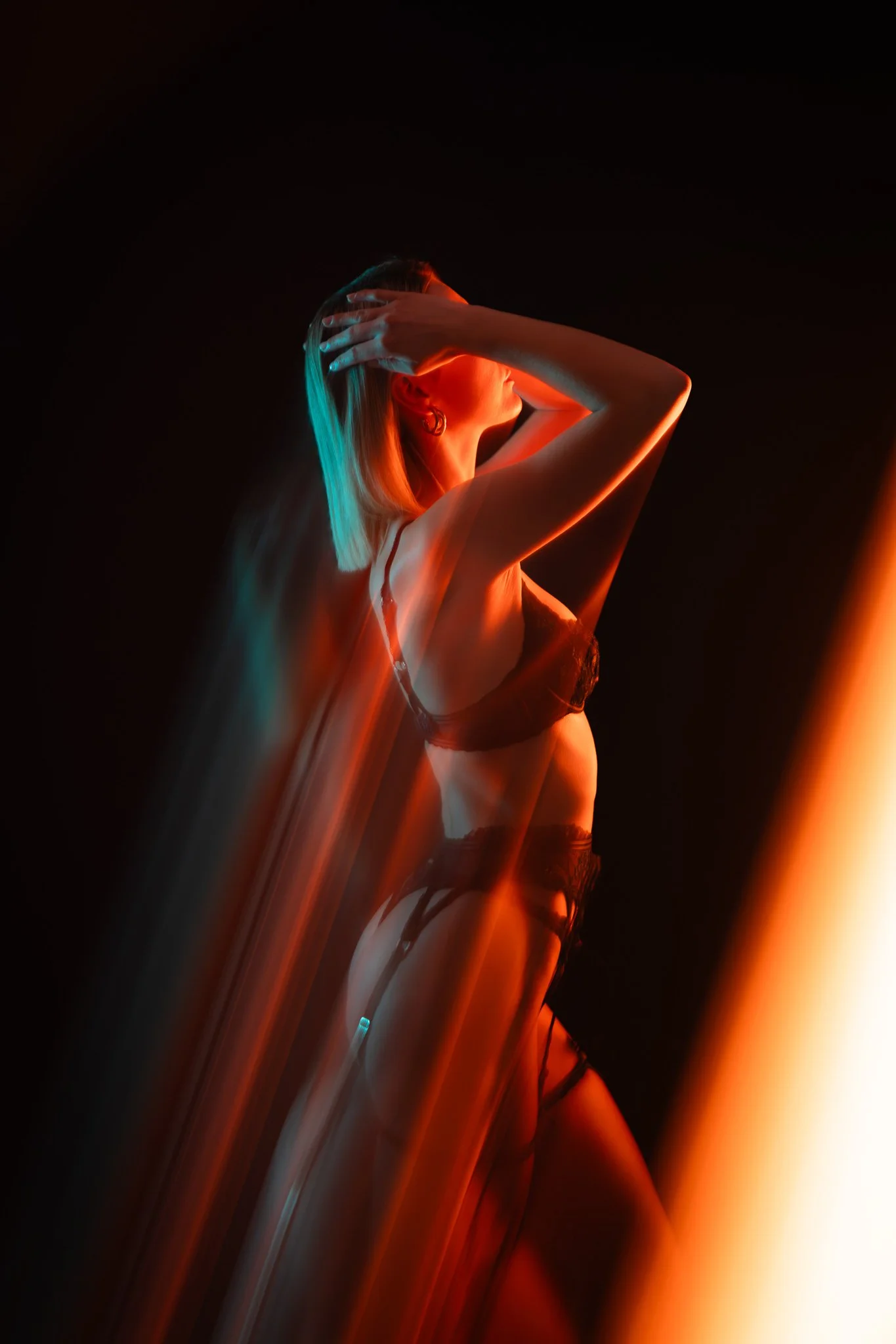 Une femme en lingerie noire, posant dans un environnement sombre avec des lumières colorées rouges et bleues, créant un effet artistique et mystérieux.
