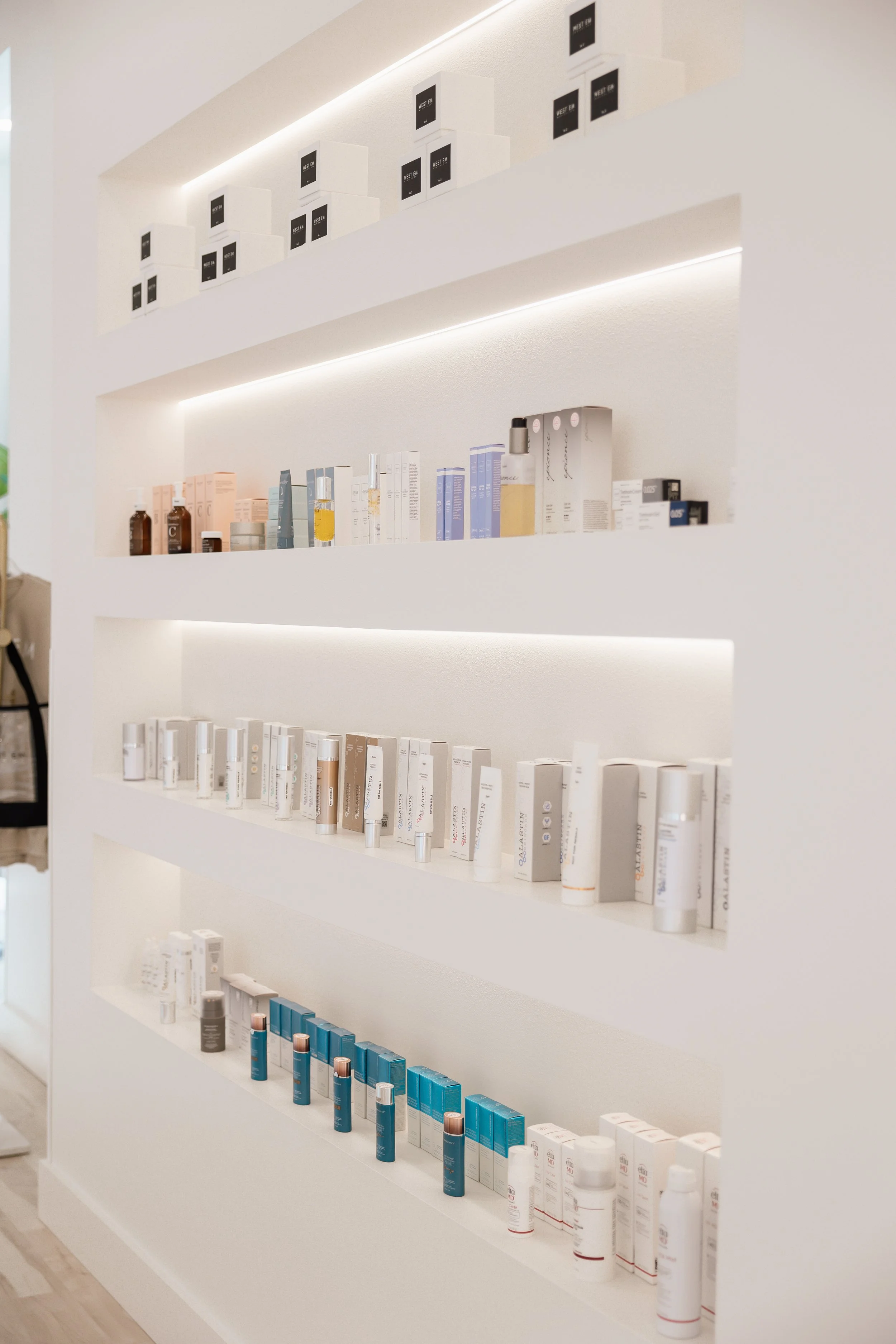 Skincare products displayed on shelves in the West Em Medical Spa lobby, featuring Epionce, Alastin, Colorescience, Face Reality, One Love Organics, and Obagi.