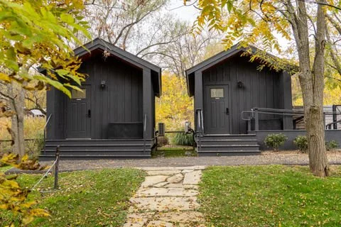 Two treatment rooms with steps leading up to doors, situated among trees with autumn foliage, and a stone pathway in front, located in the spa garden.