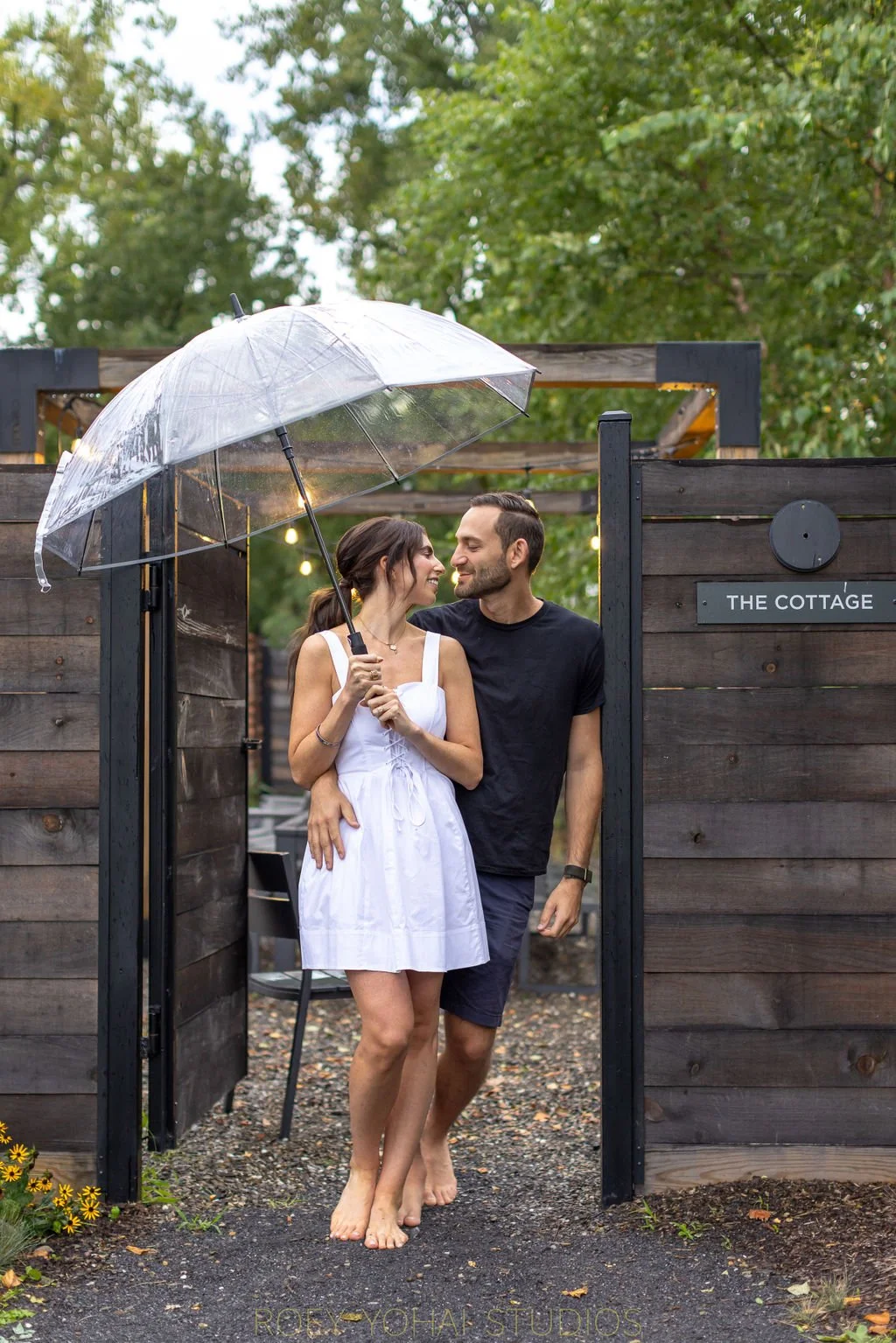  Bride and groom pose for a photo with a clear umbrella near the cottage at Hutton Brickyards 
