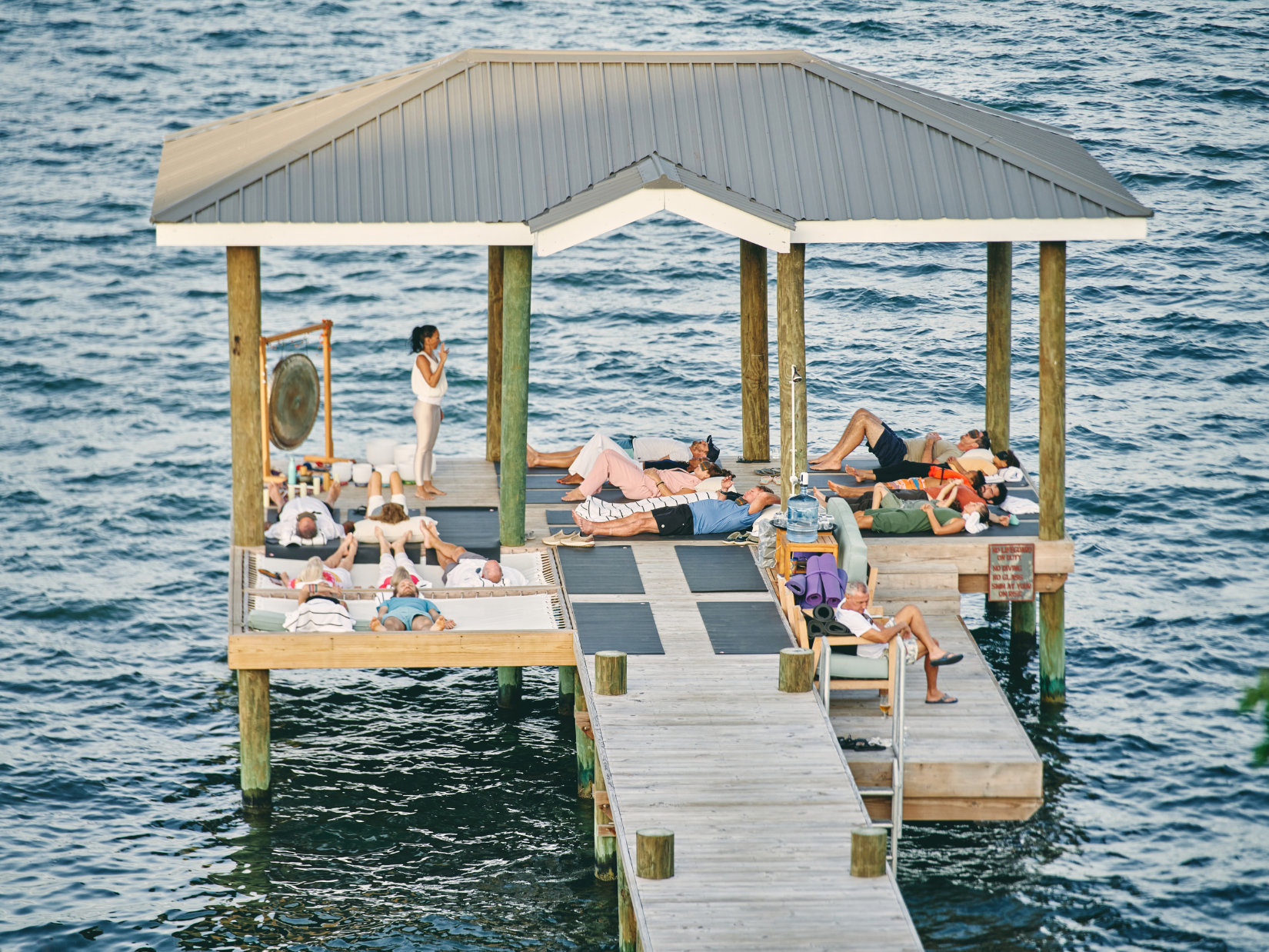 Retreat guests resting on mats in a covered pavilion at the end of a pier over the Caribbean Sea at Prana Maya, Belize
