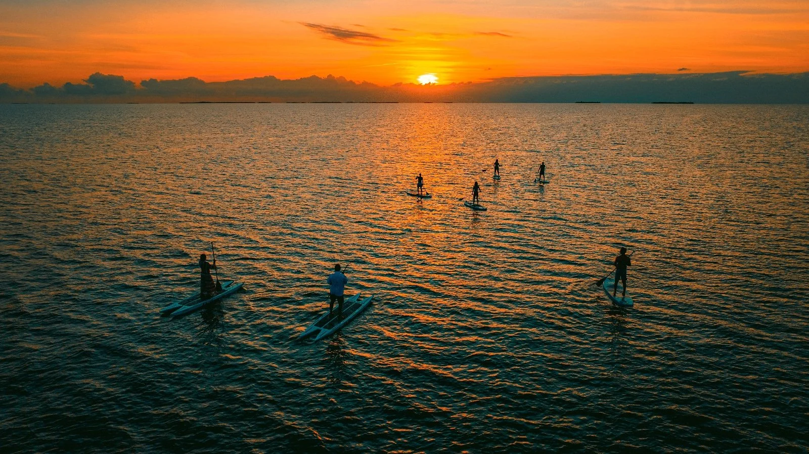 Paddleboarders gliding across calm water at sunset off Prana Maya Island Resort in Belize