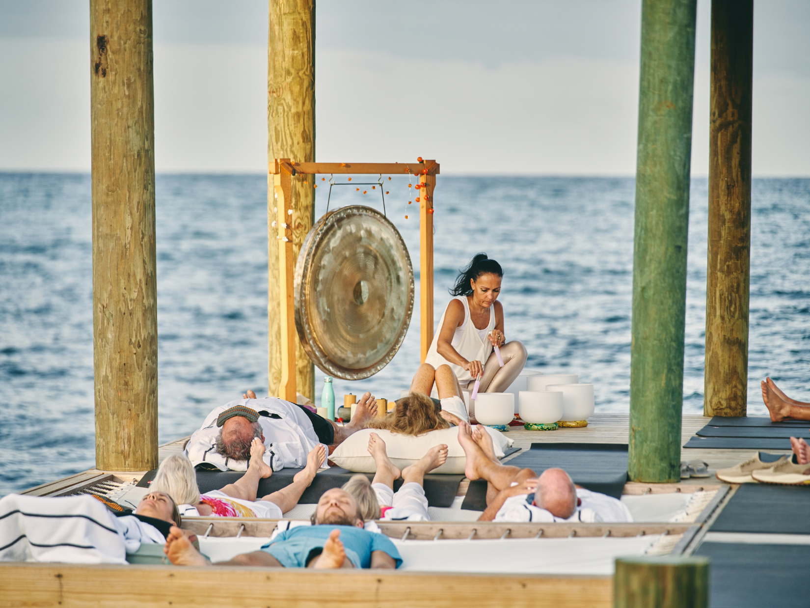 Sound healing session with a gong and crystal singing bowls as guests rest on an open-air pavilion over the sea