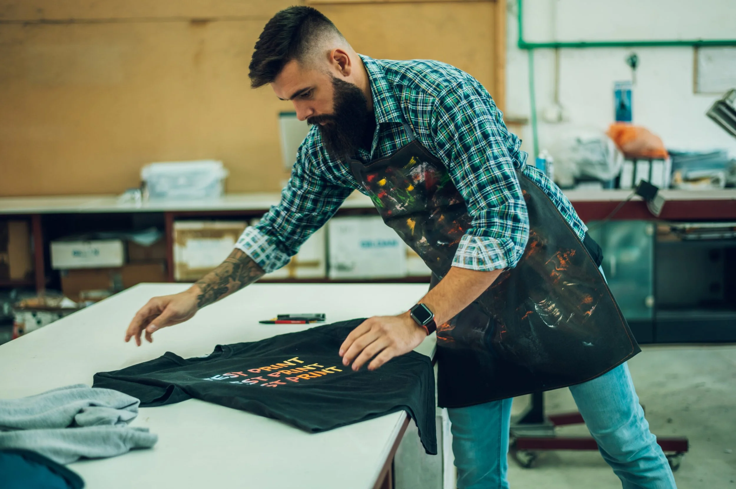 male-worker-folding-a-fresh-printed-t-shirt-in-a-p-2023-11-27-05-17-42-utc-scaled.jpg