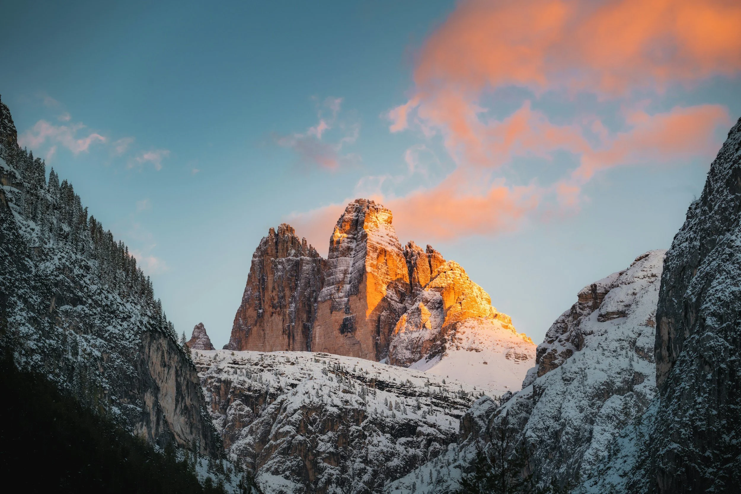 Sunset illuminating the snow-covered mountain peaks of the Tre Cime di Lavaredo in the Dolomites, with pink clouds in the sky.