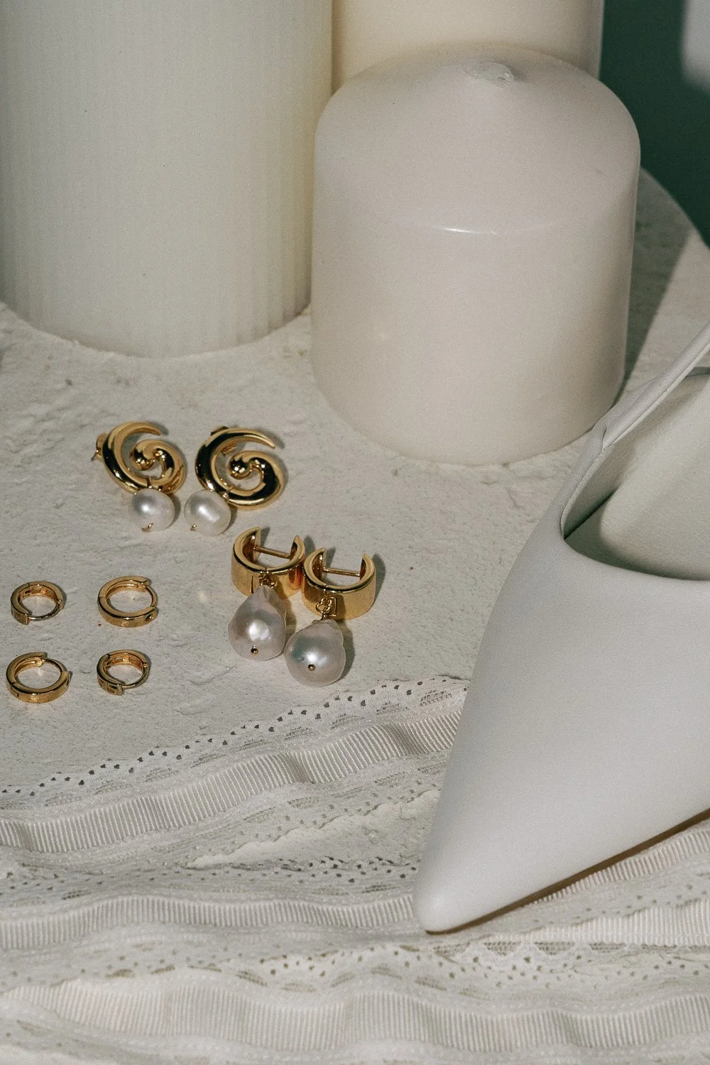 Set of gold and pearl earrings and rings on lace fabric beside a white container and a tissue box.