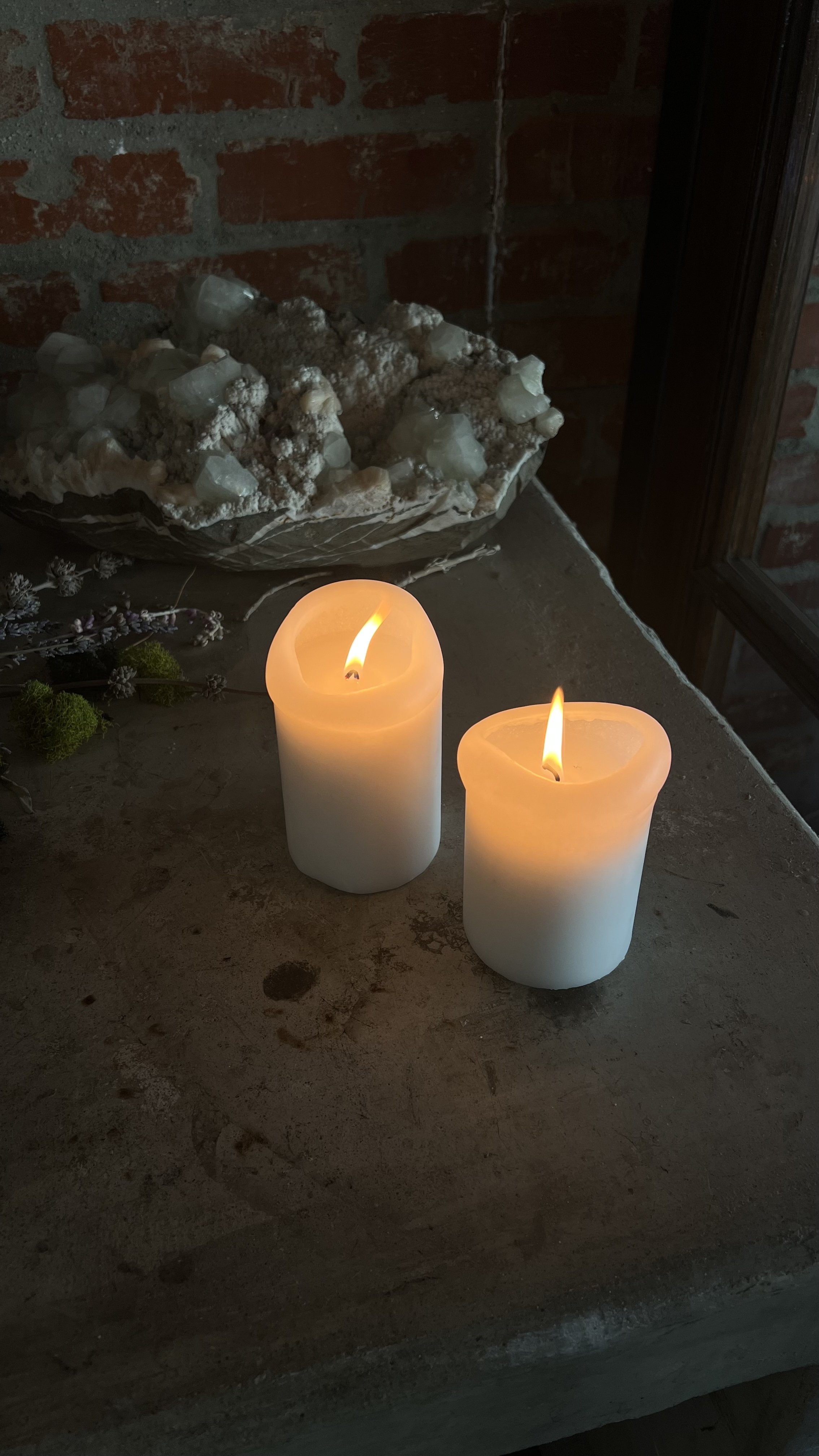 Two white flickering candles on a stone surface with a decorative crystal arrangement in the background at Golden Mean Acupuncture in Echo Park, Los Angeles CA , treatment by Rein Short, LAc.