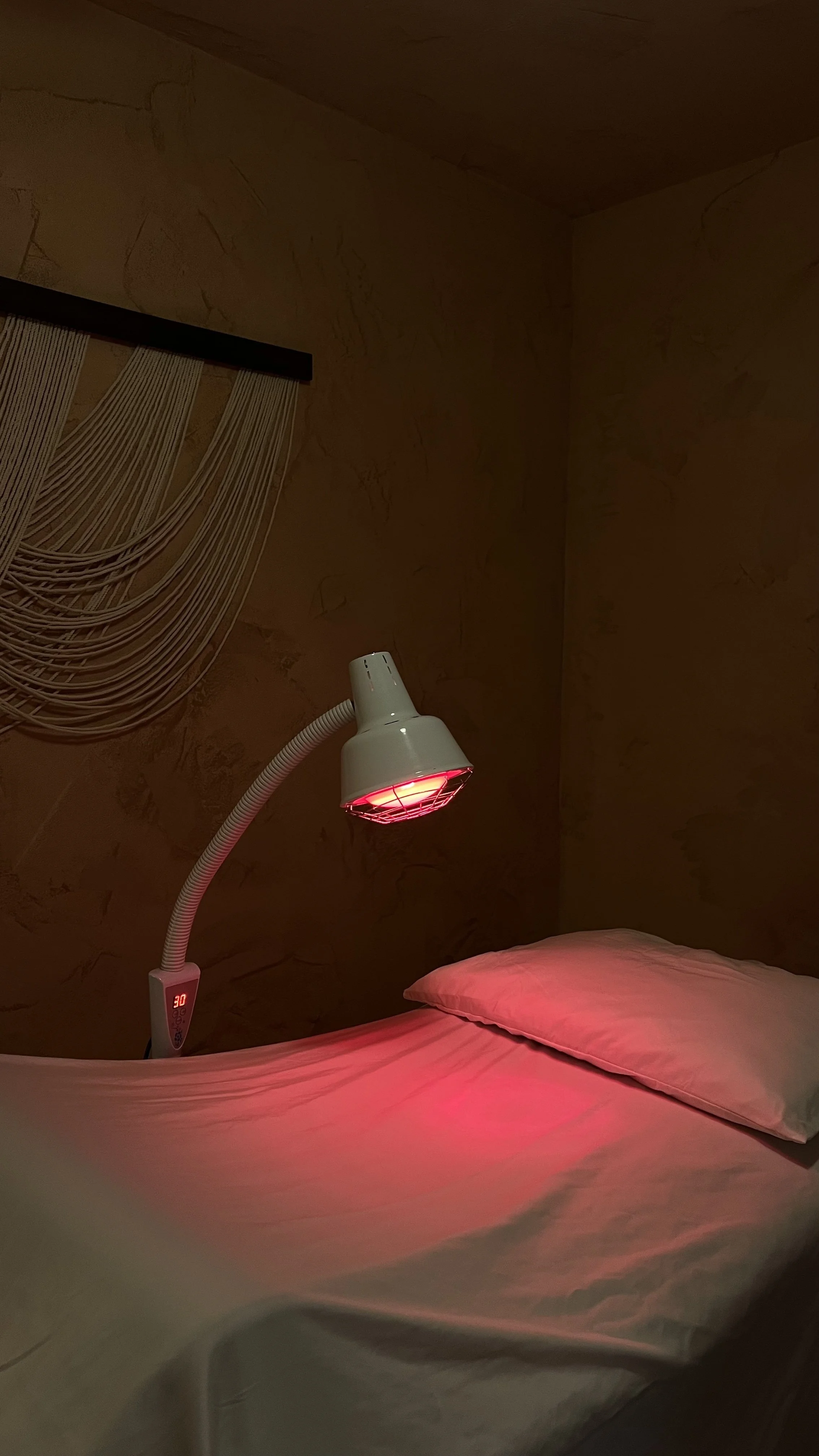 A acupuncture clinic room at Highland Holistic in Highland Park, CA with white sheets and pillows and a red infrared heat lamp, treatment by Rein Short, LAc.
