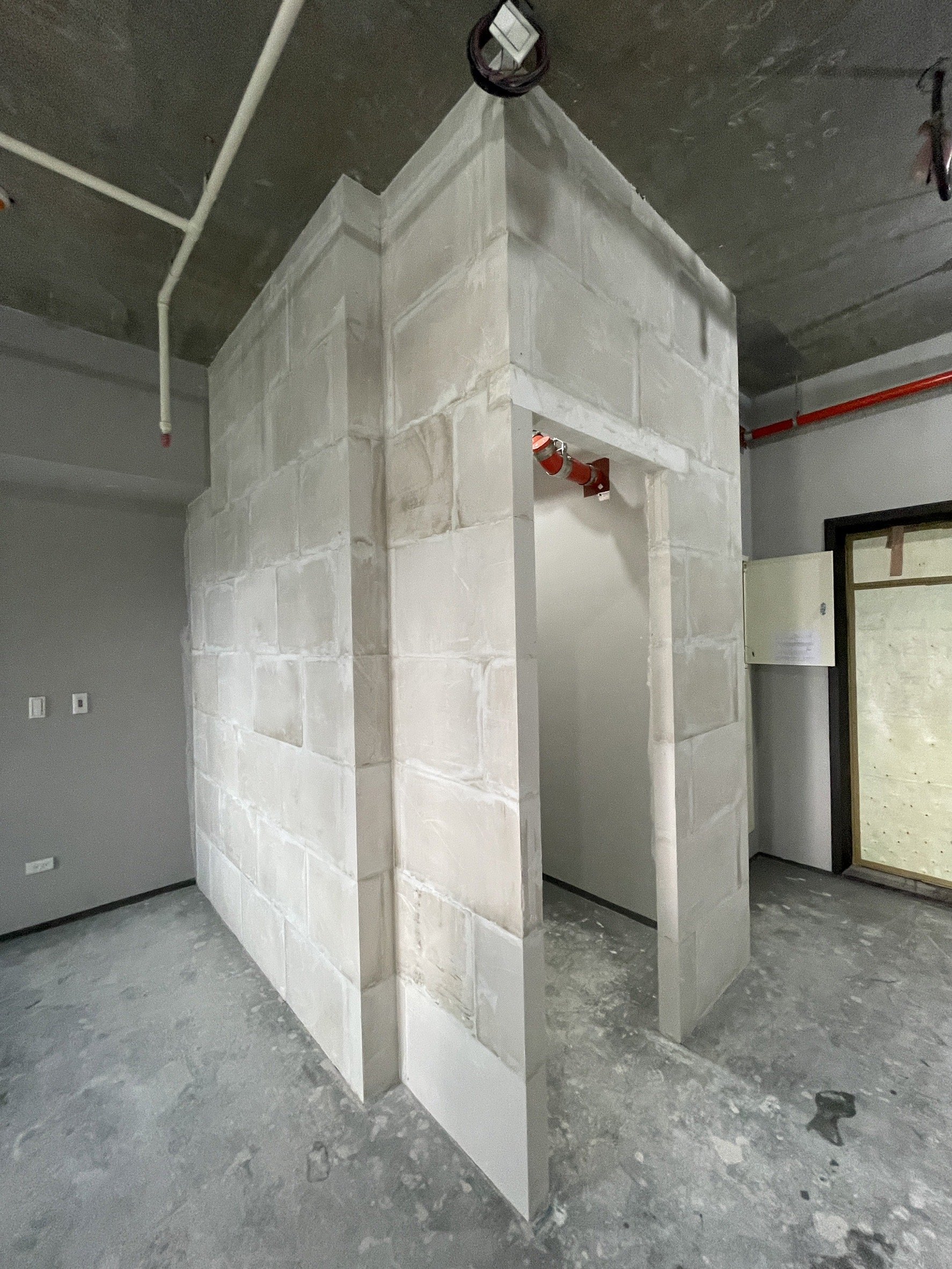 Partially constructed cement block wall with doorway and exposed pipes in an unfinished interior space.