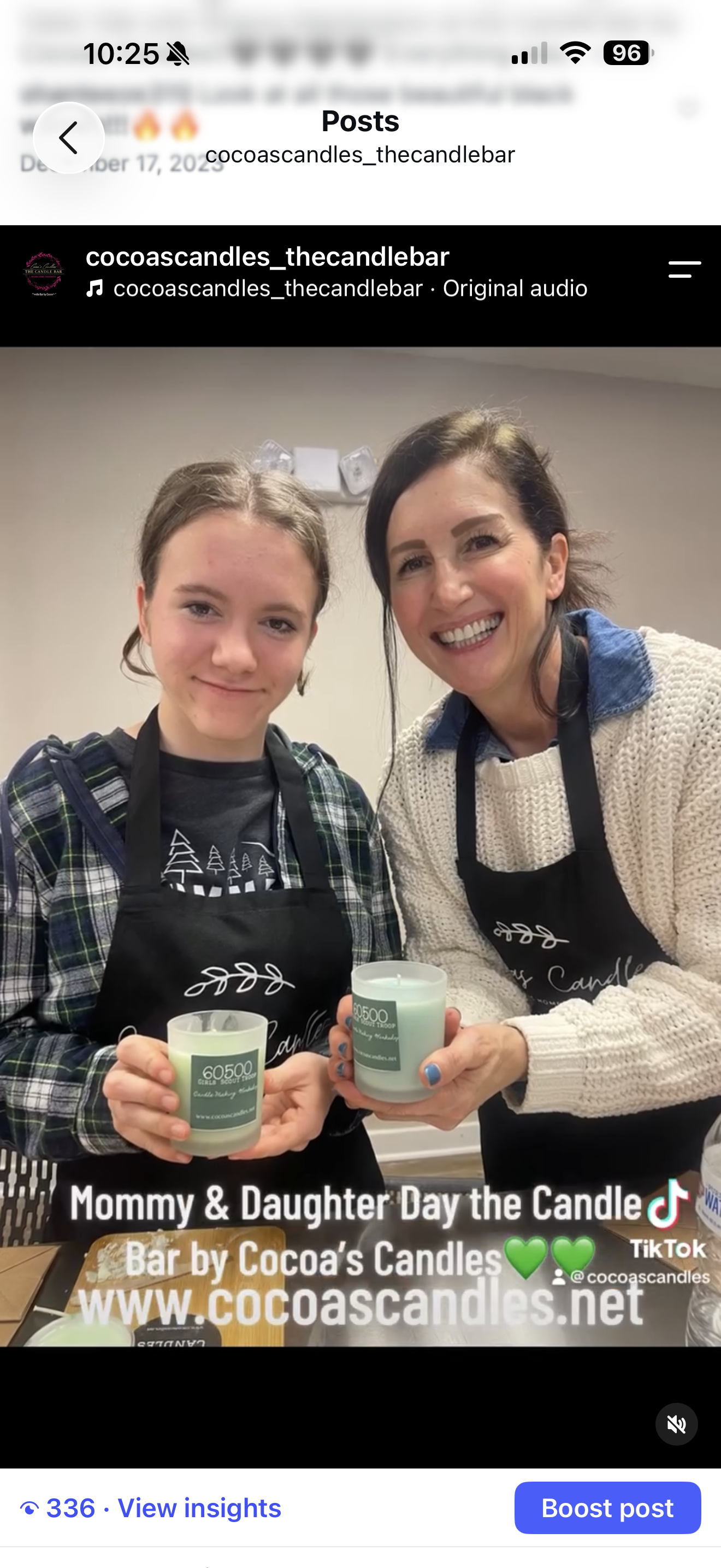 Mommy and daughter smiling and holding green candles in glass holders at Cocoa's Candles event. Both wearing black aprons, with a table and candles in front of them.
