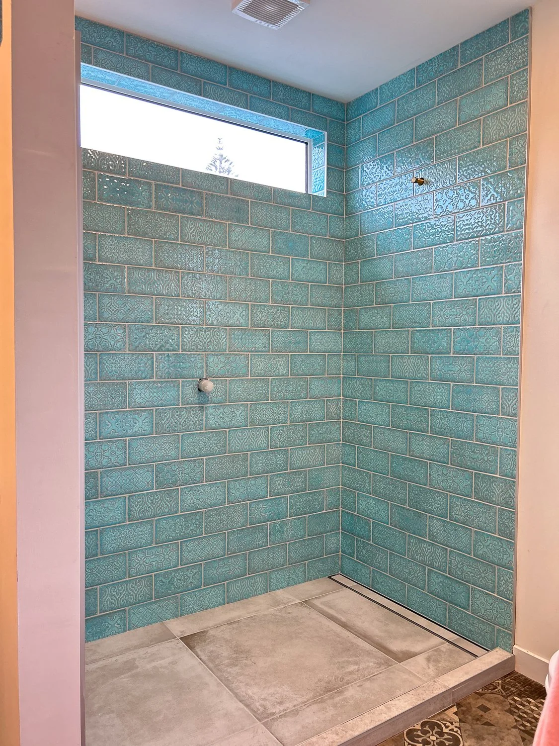 Empty shower with turquoise decorative tiles, a small window near the ceiling, and a floor drain.