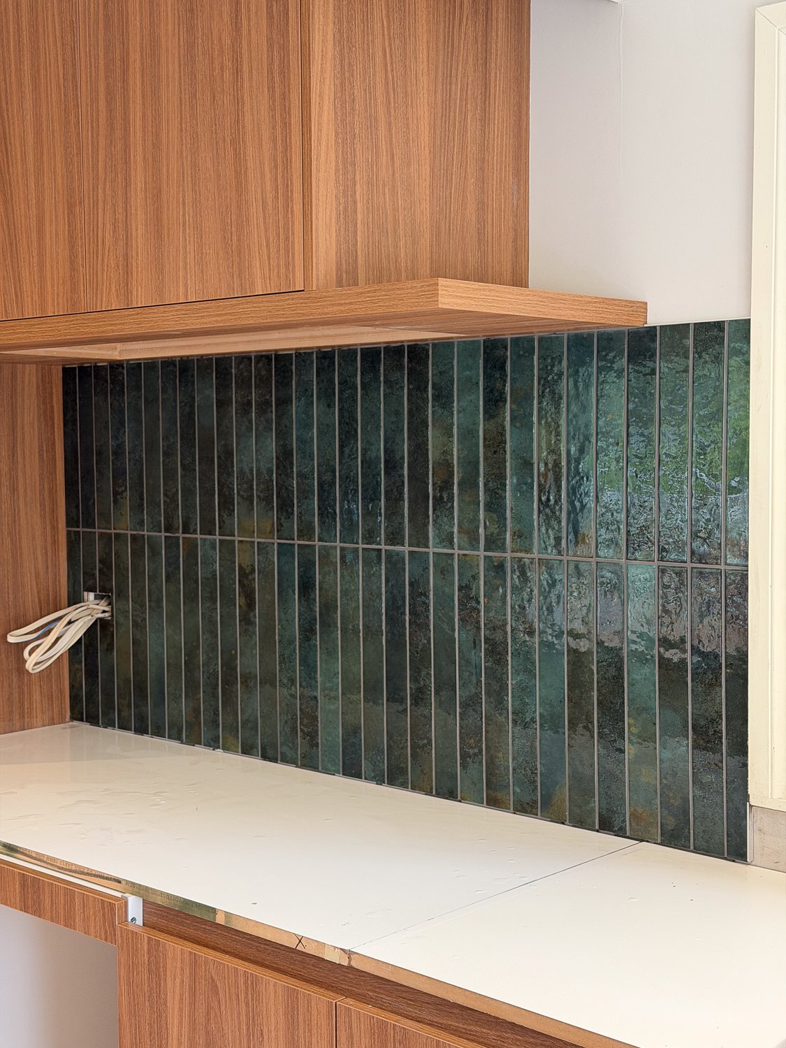 A kitchen countertop with unfinished edges, a green tiled backsplash, and wooden upper cupboards.
