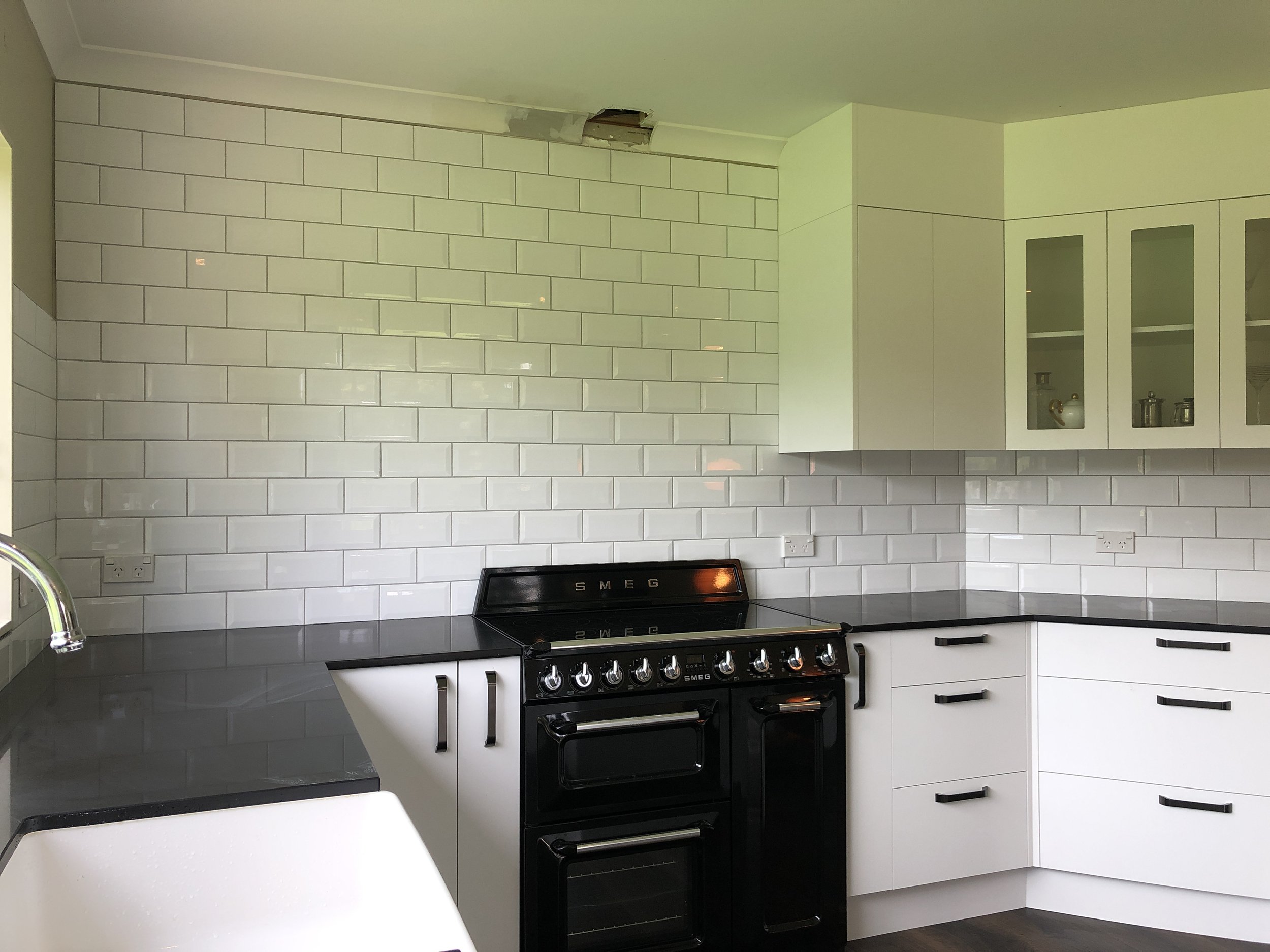 Modern kitchen with white cabinetry, subway tile backsplash, black oven, and a hole in the ceiling.