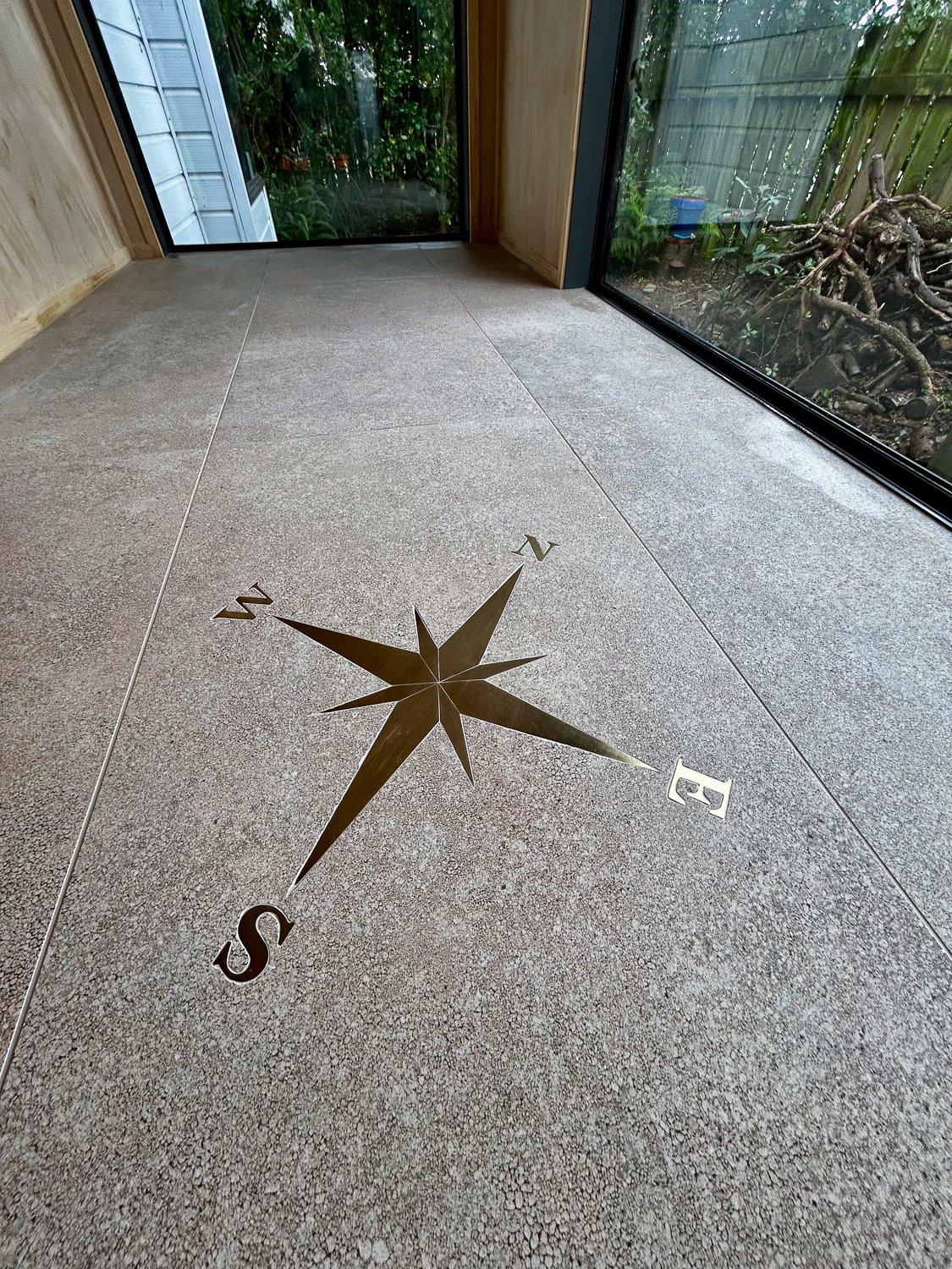 Indoor space with a floor decal of a compass rose indicating north, south, east, and west, with large windows showing outdoor greenery.