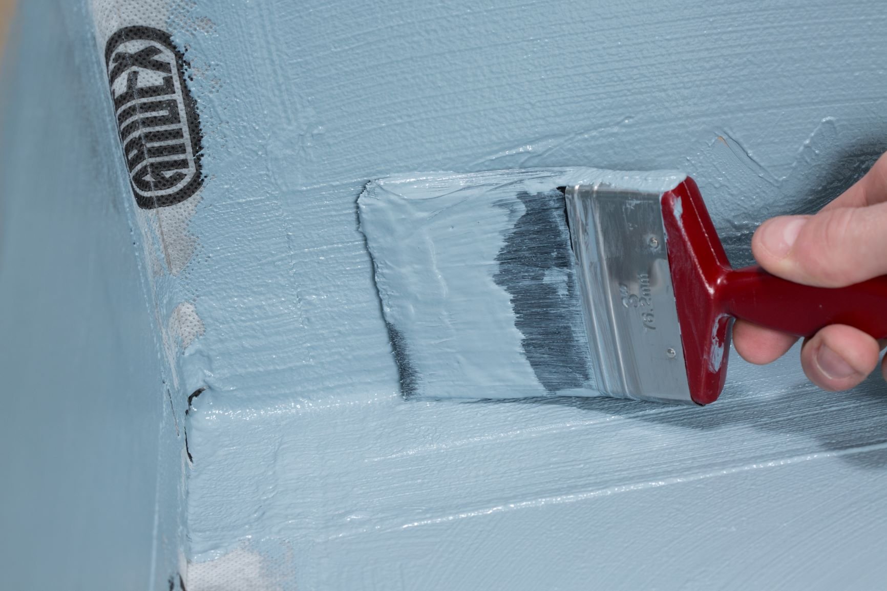 A person applying light blue paint to a wall with a flat paintbrush.