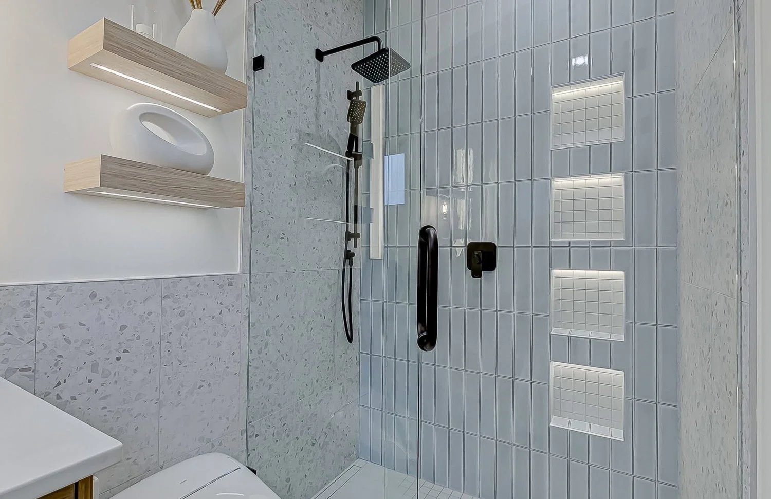 Modern walk-in shower with gray tile walls, black fixtures, built-in niche shelves, and a glass door.
