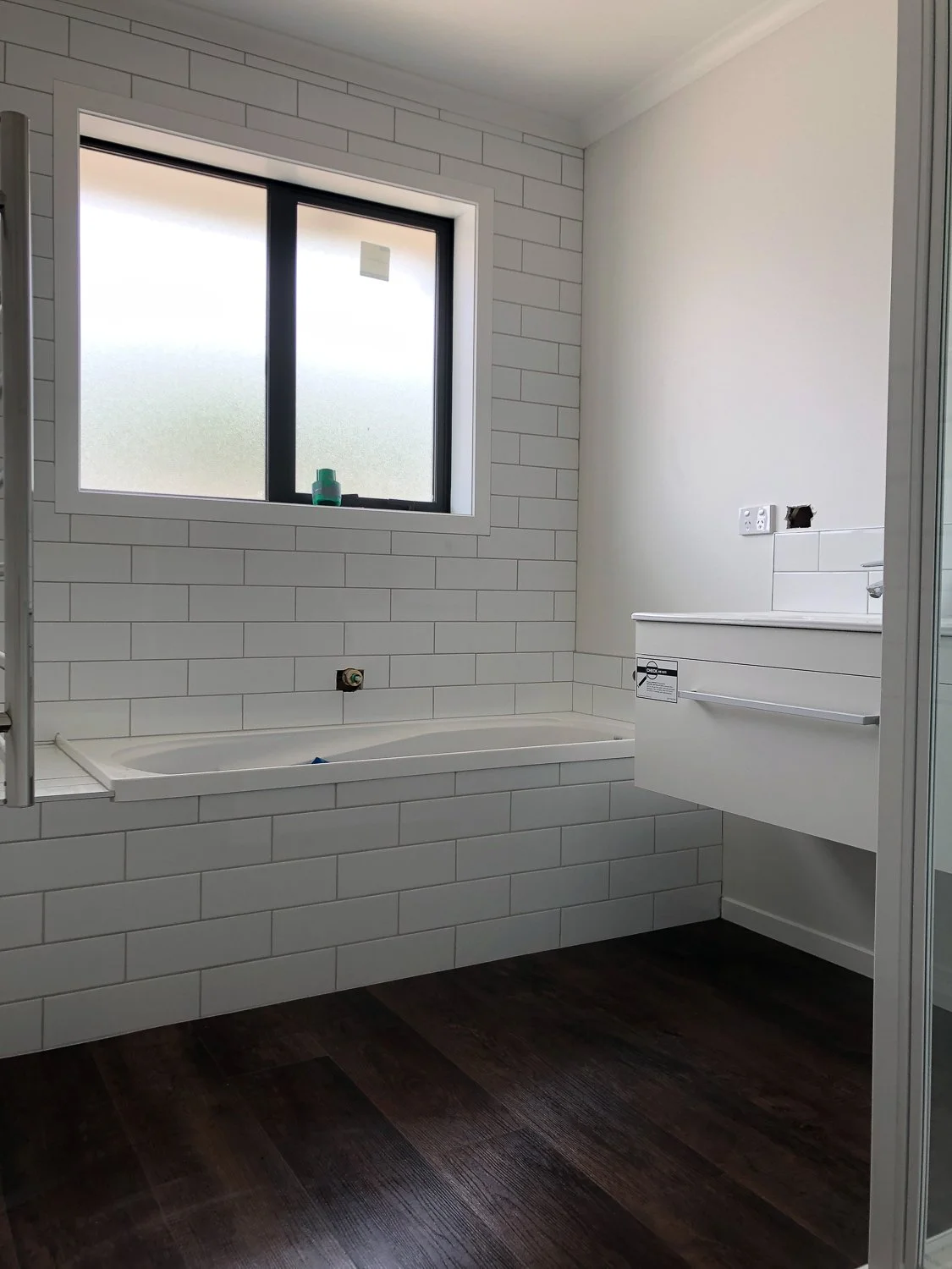 Bathroom under construction with white tiled walls, a bathtub, a frosted window, and a white floating vanity.