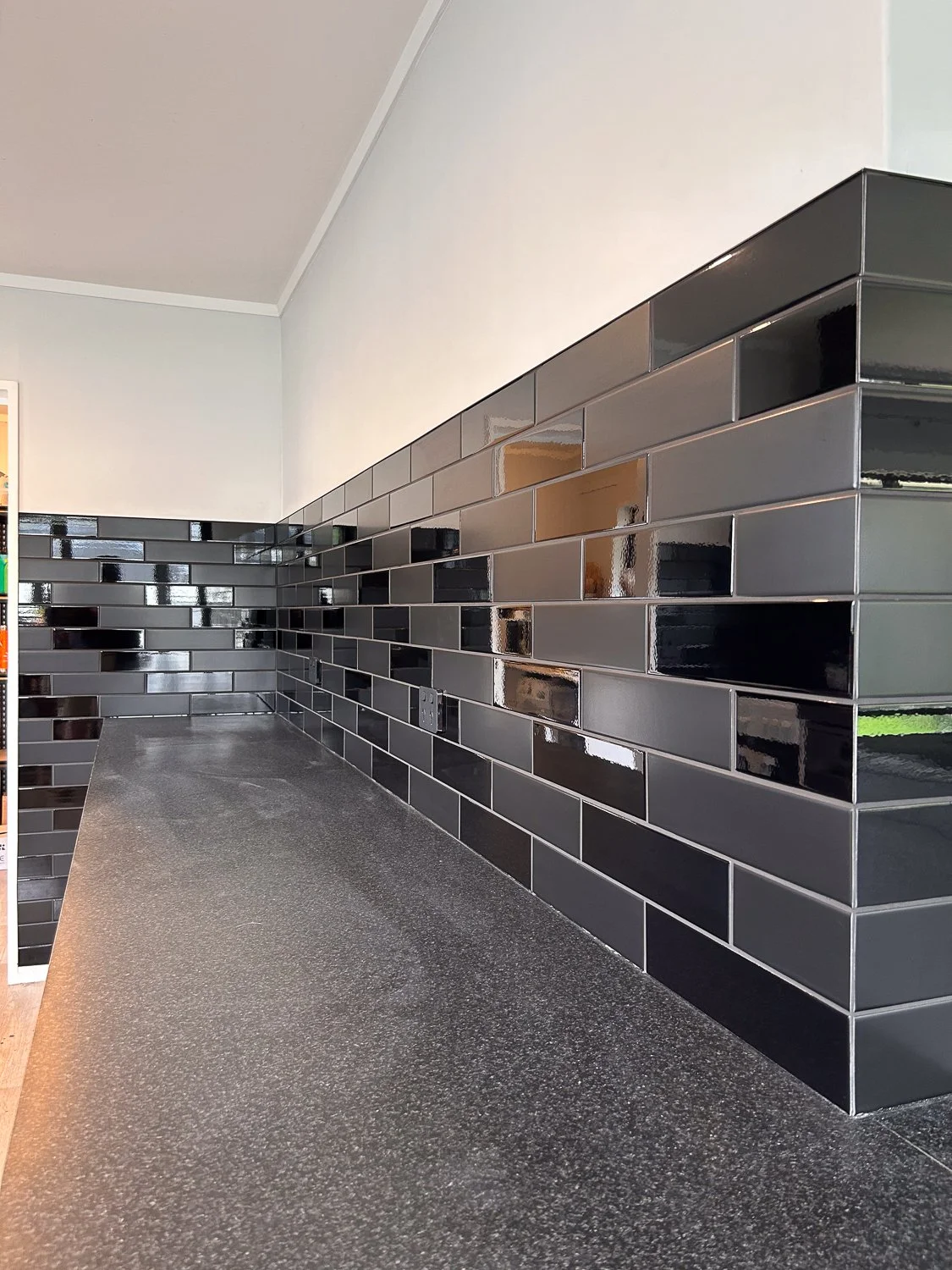 Interior view of a kitchen counter with black granite surface and a black tile backsplash with glossy rectangular tiles.