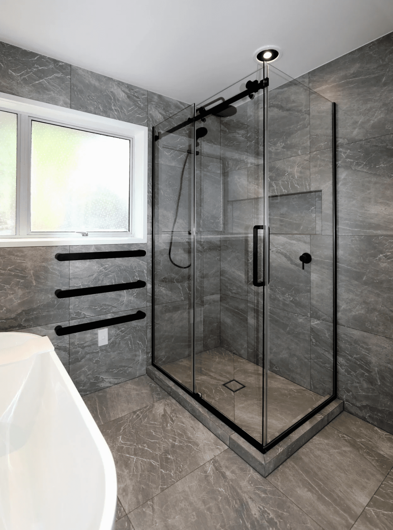 Full tiled bathroom in dark large format tiles with black framed shower