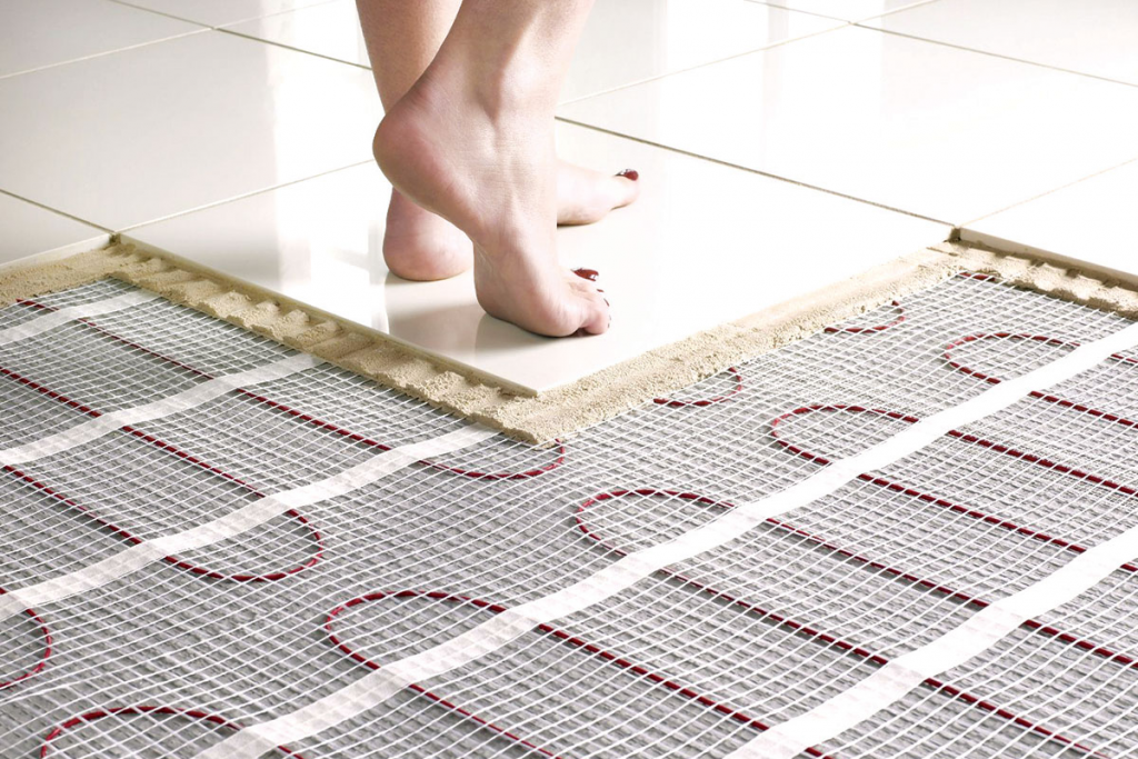 Person installing underfloor heating mats with electric wires on a tiled floor.