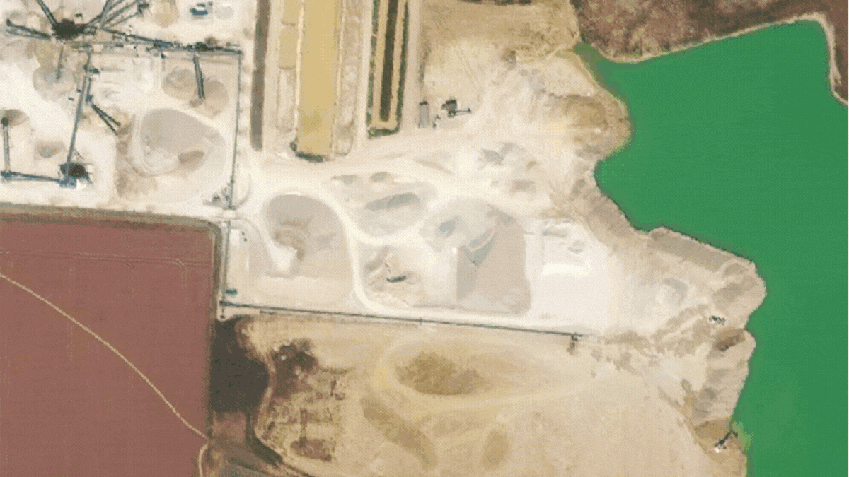 Aerial view of a construction site near a body of green water, with areas of cleared land and dirt paths, and some machinery present shows as a timeline in Plex-Earth.