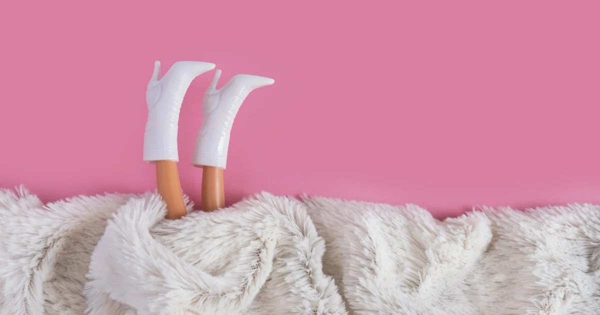 Några fötter med strumpor under ett fluffigt täcke på en rosa bakgrund.