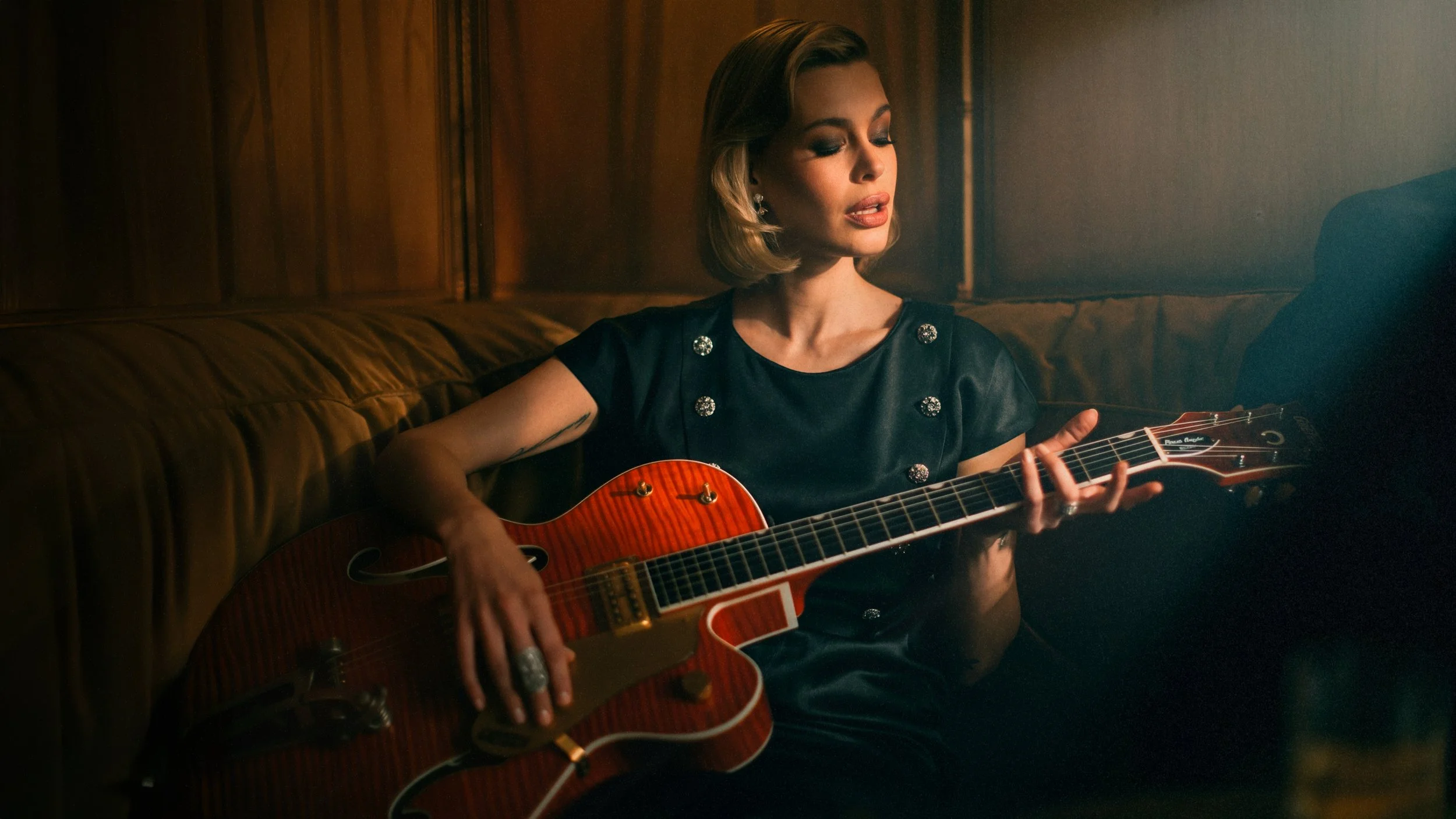 Une femme joue de la guitare acoustique dans une pièce chaleureuse et sombre.