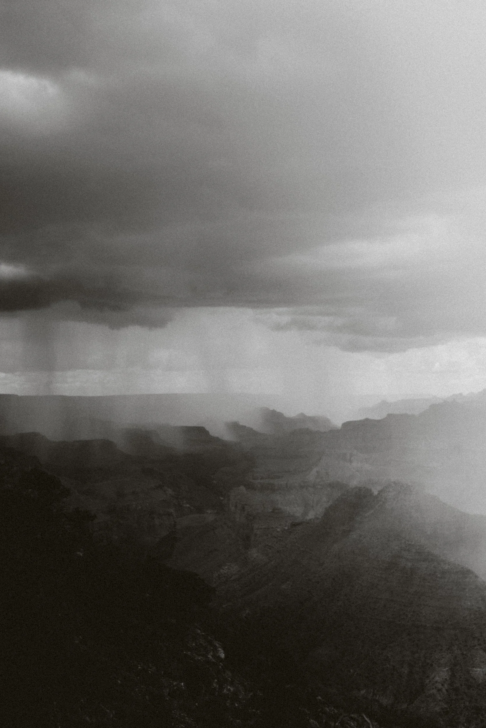 Paysage montagneux avec ciel nuageux sombres et pluie visible à l'horizon.
