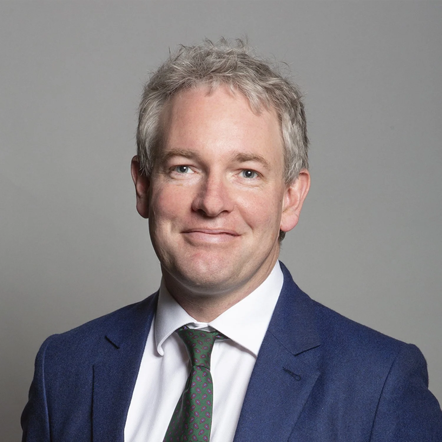 Official Portrait of Danny Kruger. A head and shoulders framing, he has a blue suit jacket and green tie. He has short slightly tousled hair and smiles at the camera.