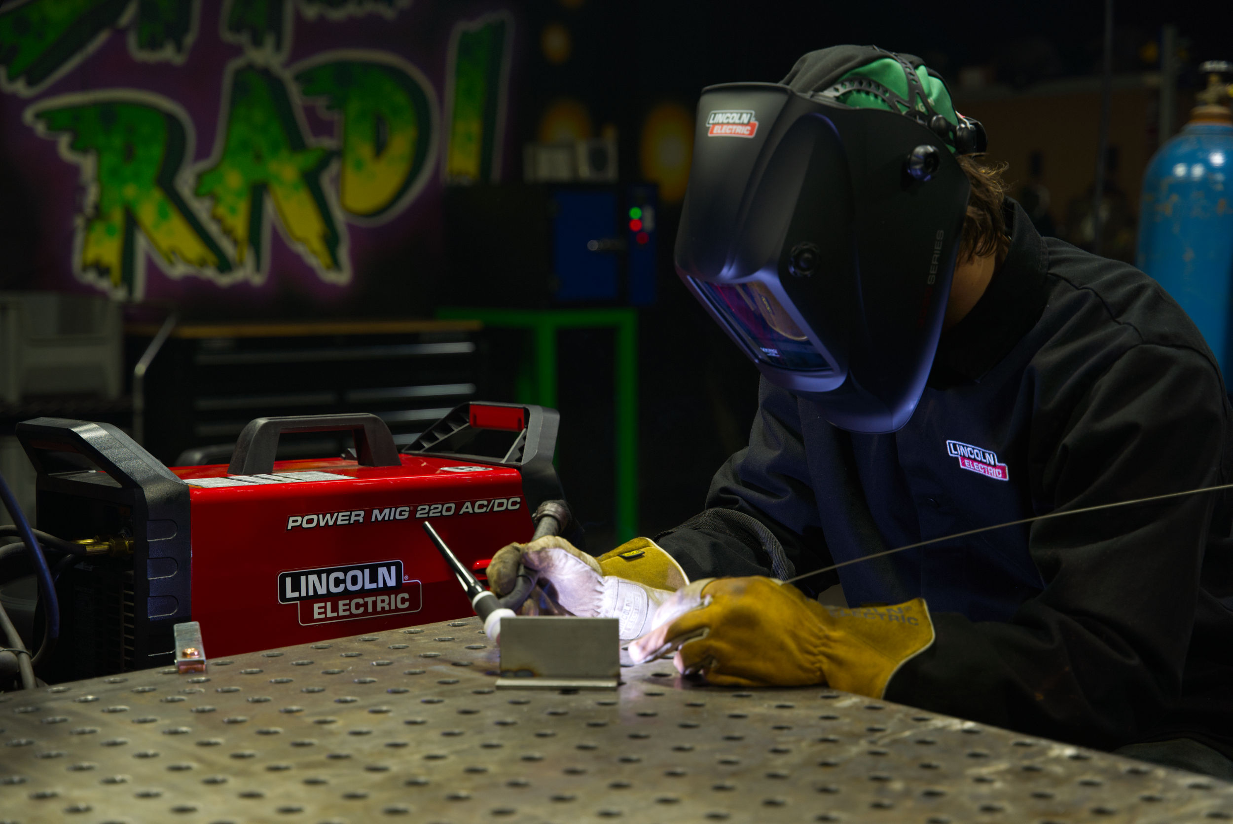 A welder in protective gear using a welding torch in a workshop, with bright sparks and tools visible.