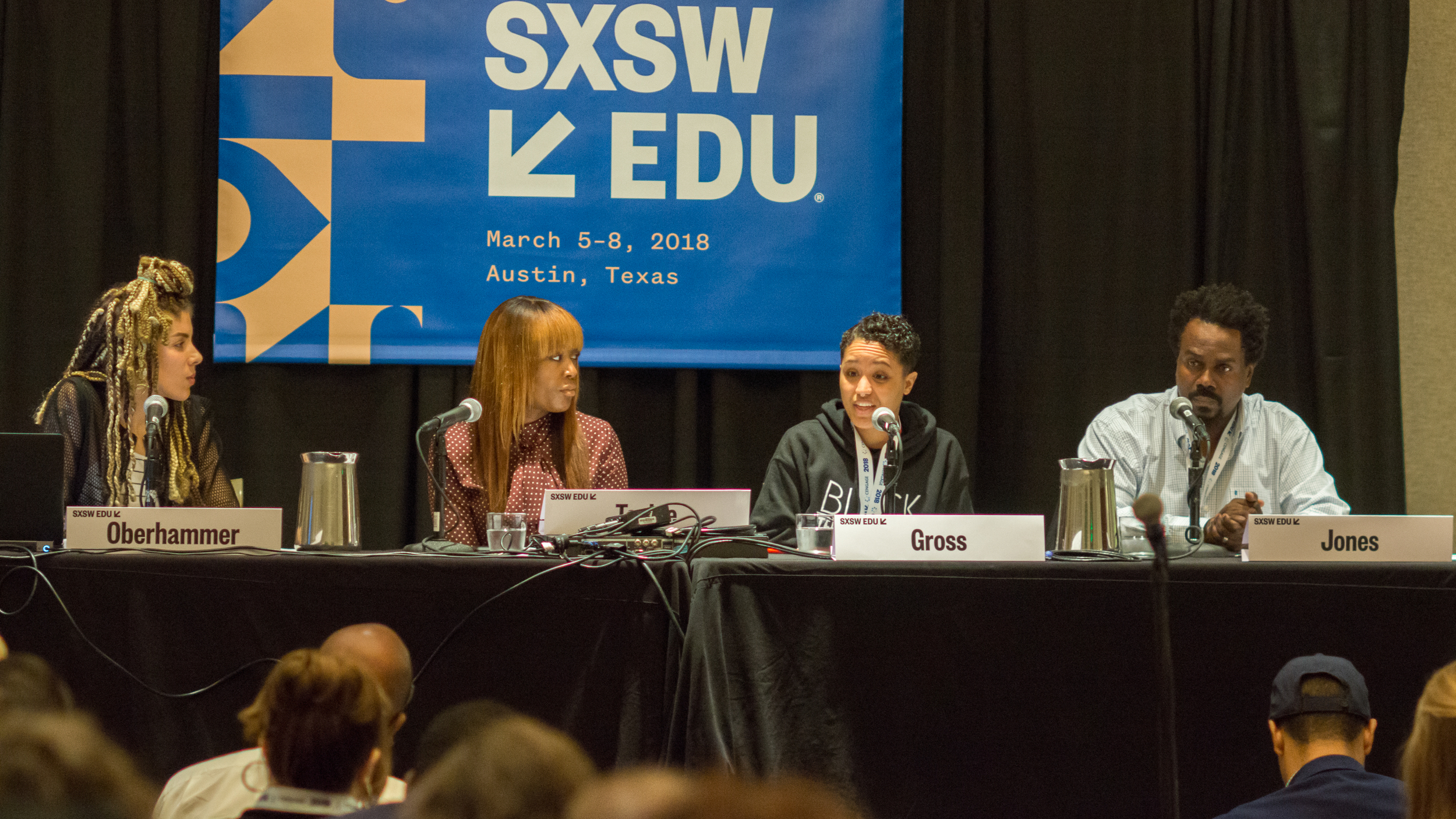 Panel of four people sitting behind a table with microphones, participating in a discussion at SXSW EDU 2018, held in Austin, Texas from March 5-8. The panelists are identified by name tags, and a large blue SXSW EDU banner hangs behind them.