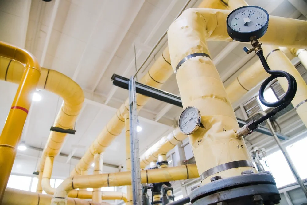 Tuberías amarillas con aislamiento y manómetros en el techo de una fábrica para sistemas de enfriamiento industrial.
