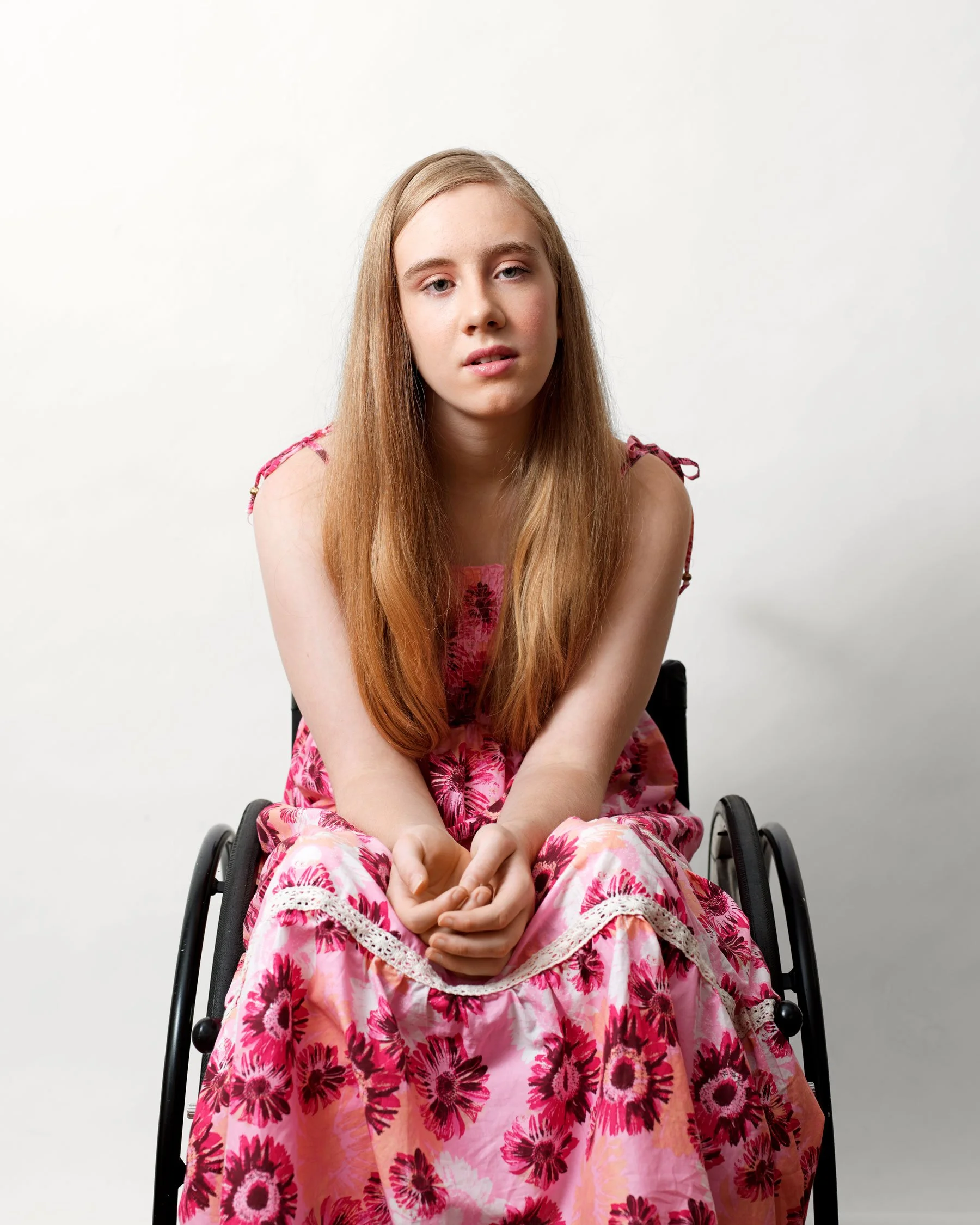 Portrait of a girl (Andie) with Cerebral Palsy sitting in a wheelchair and wearing a pink floral dress by photographer David.A.Knight. The portrait was selected as a finalist in the Taylor Wessing and hung in The British National Portrait Gallery ©