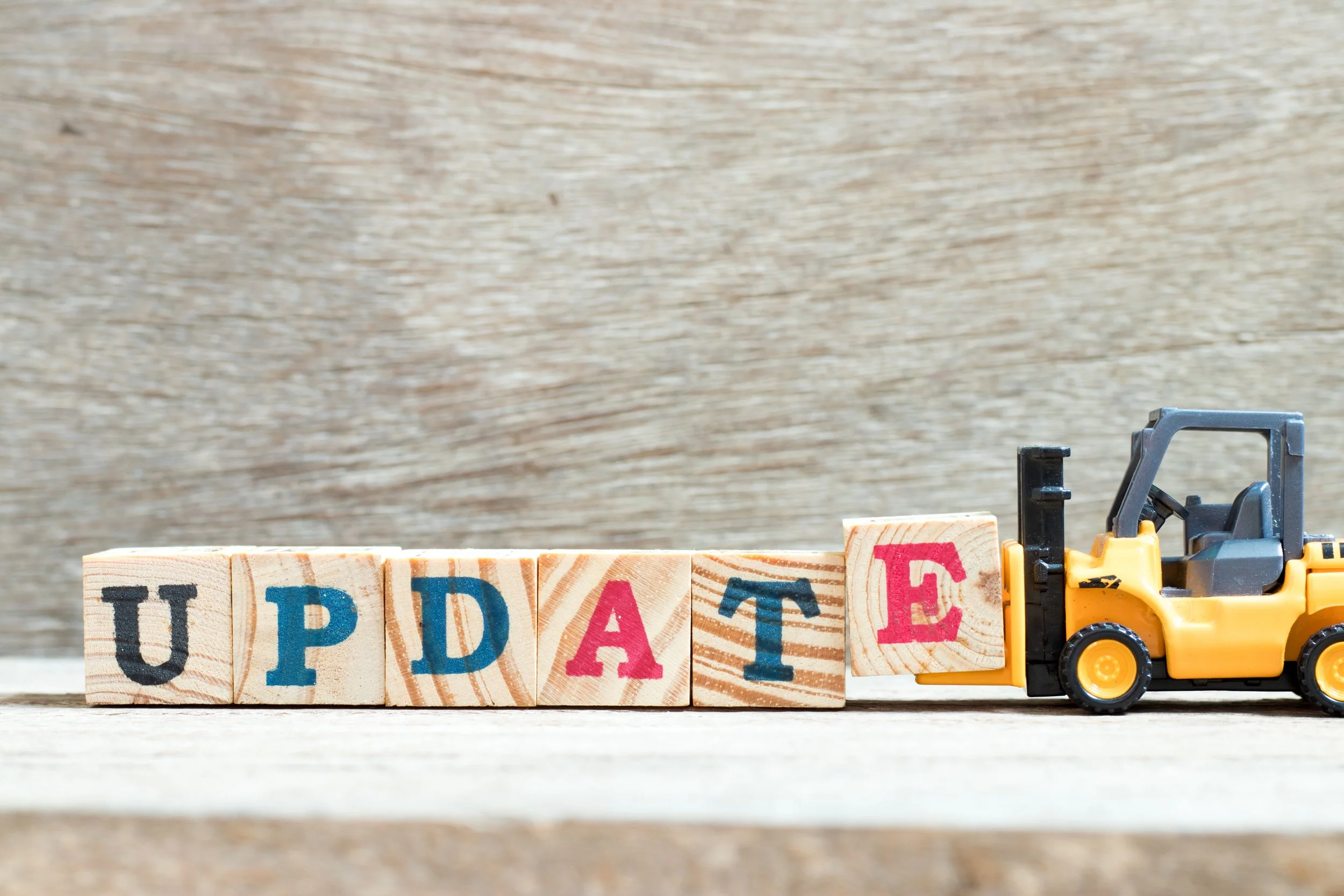 Colorful wooden blocks spelling 'UPDATE' with a miniature forklift truck pushing the last block.