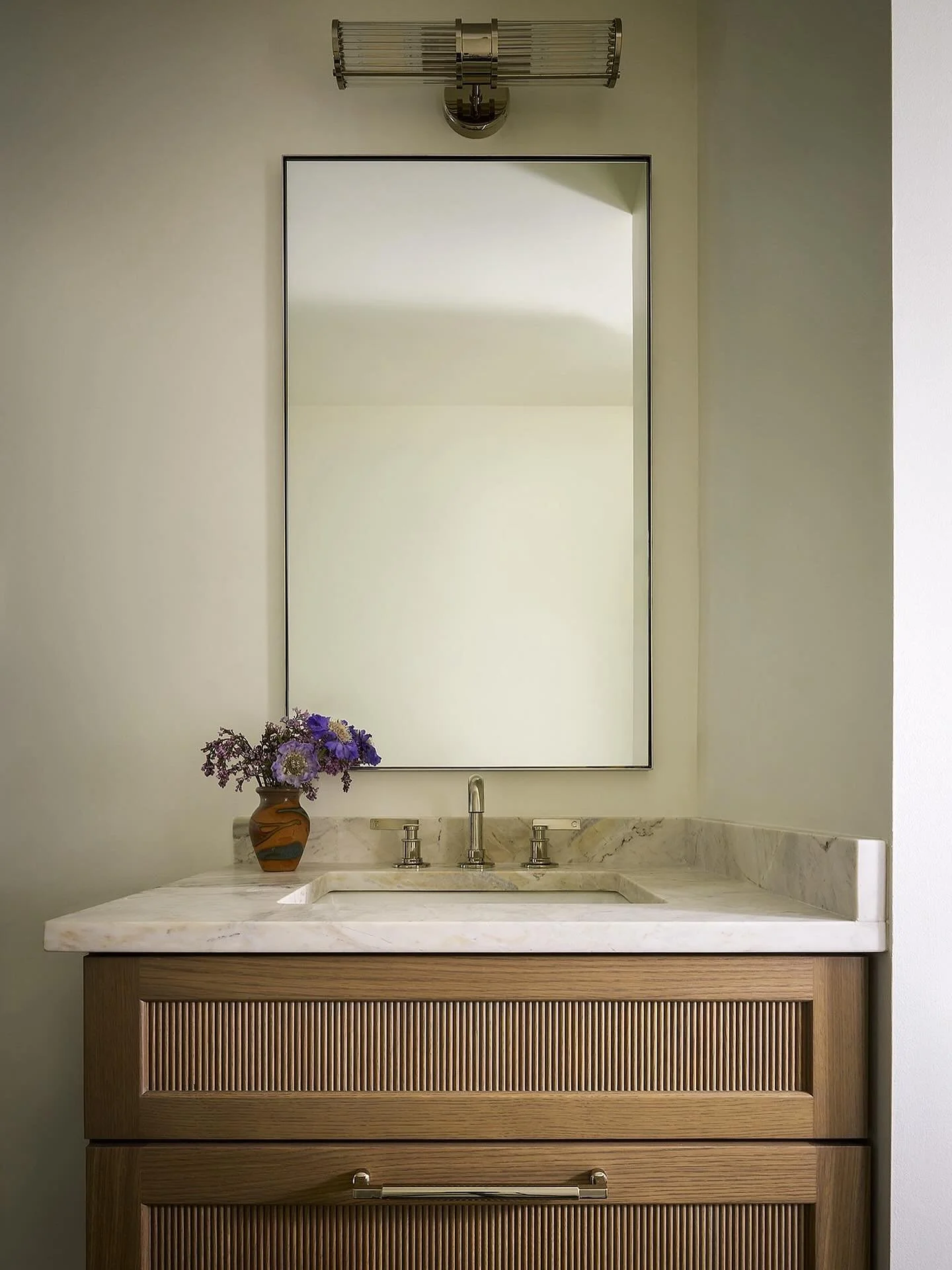 Quiet luxury meets thoughtful design.✨This powder room captures understated beauty  through every detail &mdash; from custom reeded cabinetry echoed in the glass sconces, to polished nickel hardware and luxe marble finishes.

Photo: @rymcdon
Florals: