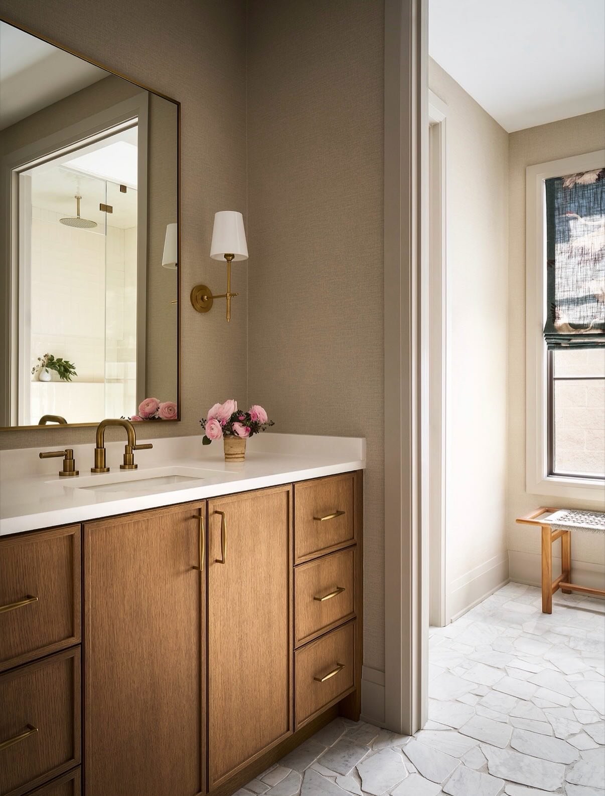 Designed with intention from top to bottom, this Bucktown primary bath features organic-shaped Carrara marble and handcrafted subway tile extending to the shower ceiling, layered with textured wallcovering and antique brass accents for a serene, spa-